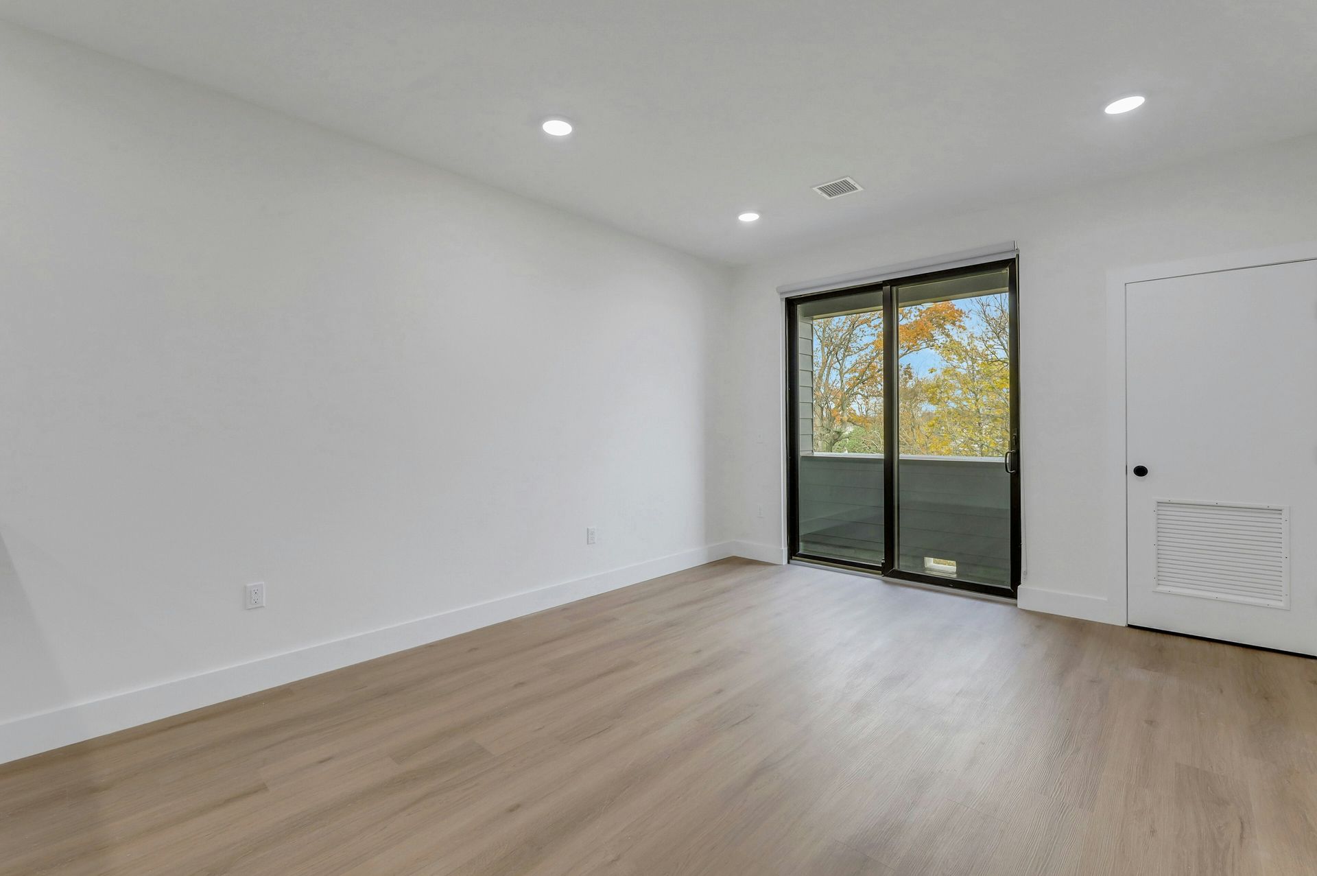 Empty room with light wood floors, white walls, sliding glass door, and a white door.