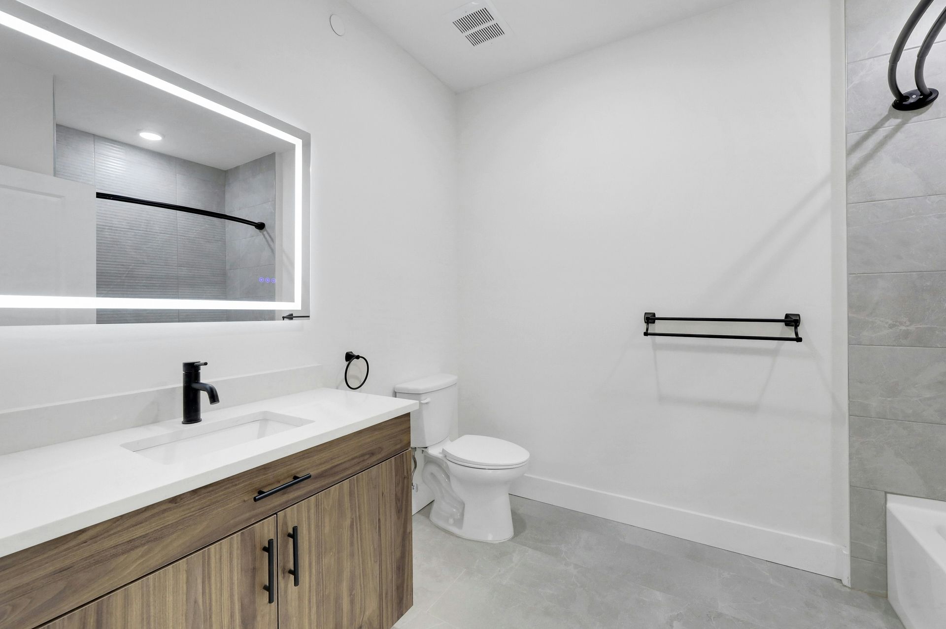 Modern bathroom with vanity, toilet, and shower. White walls, grey floor, and wooden vanity cabinet.