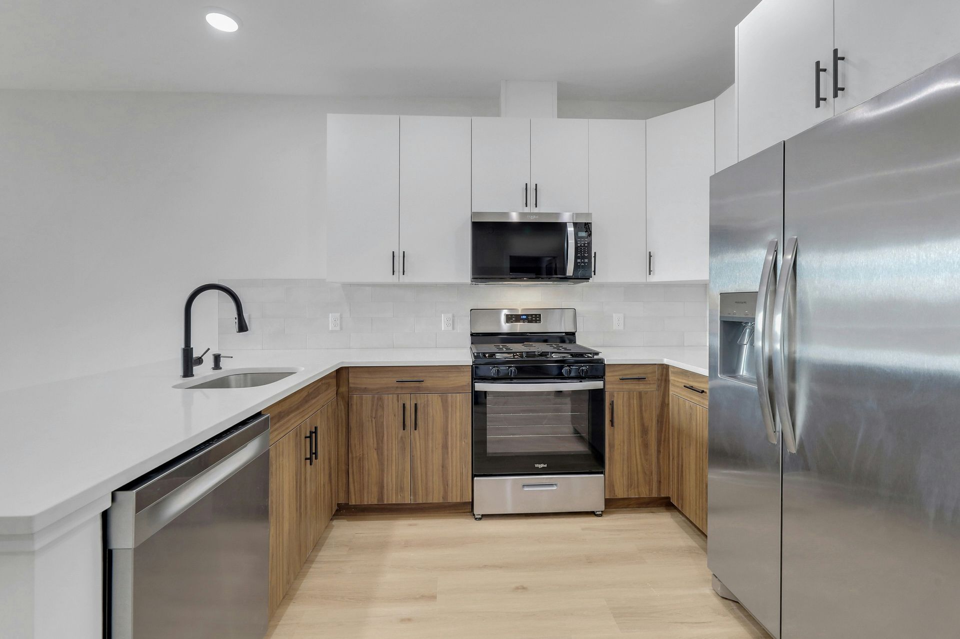 Modern kitchen with white and wood cabinets, stainless steel appliances, and light wood flooring.