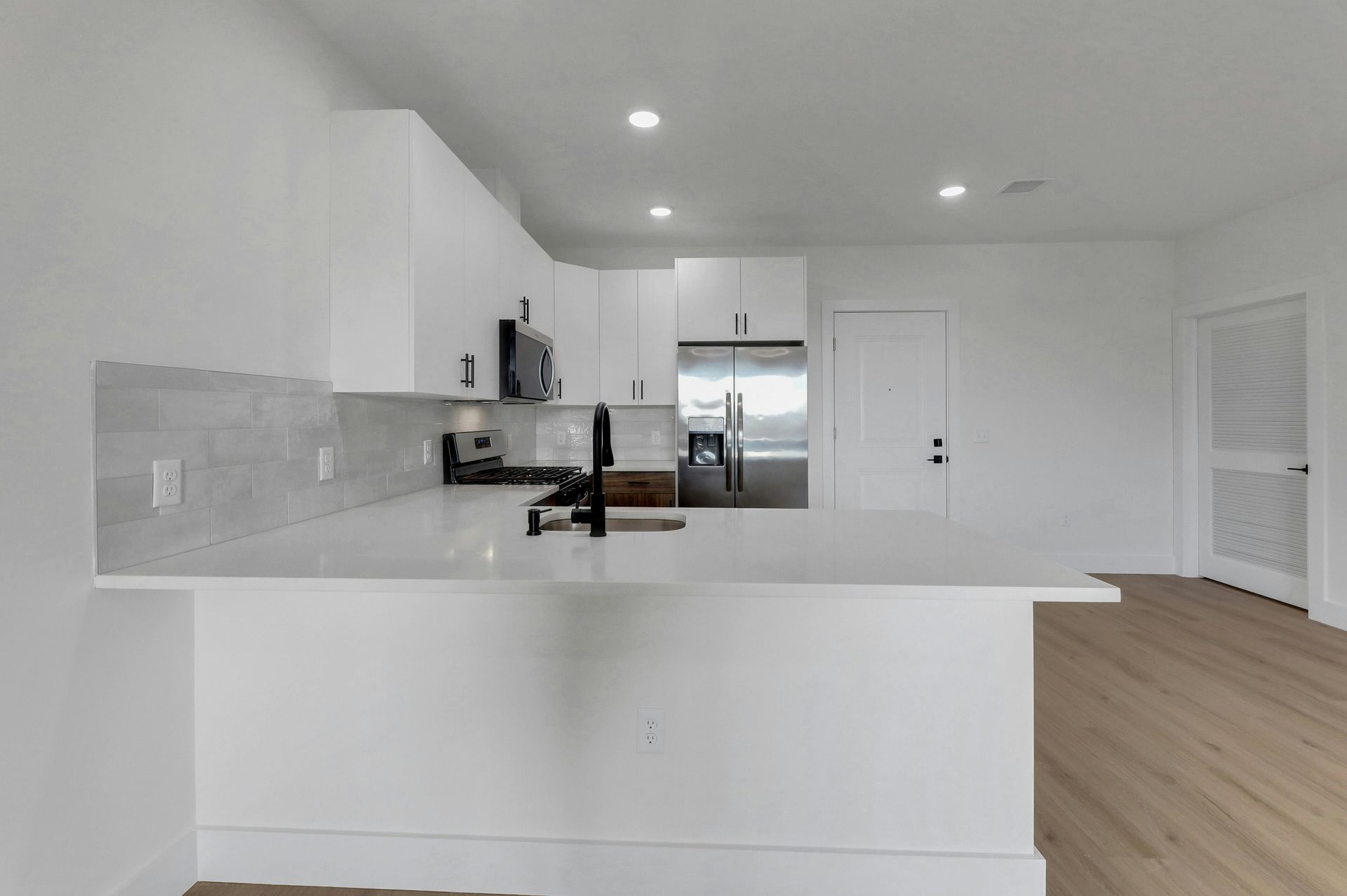 Modern white kitchen with island, cabinets, appliances, and light wood floors.