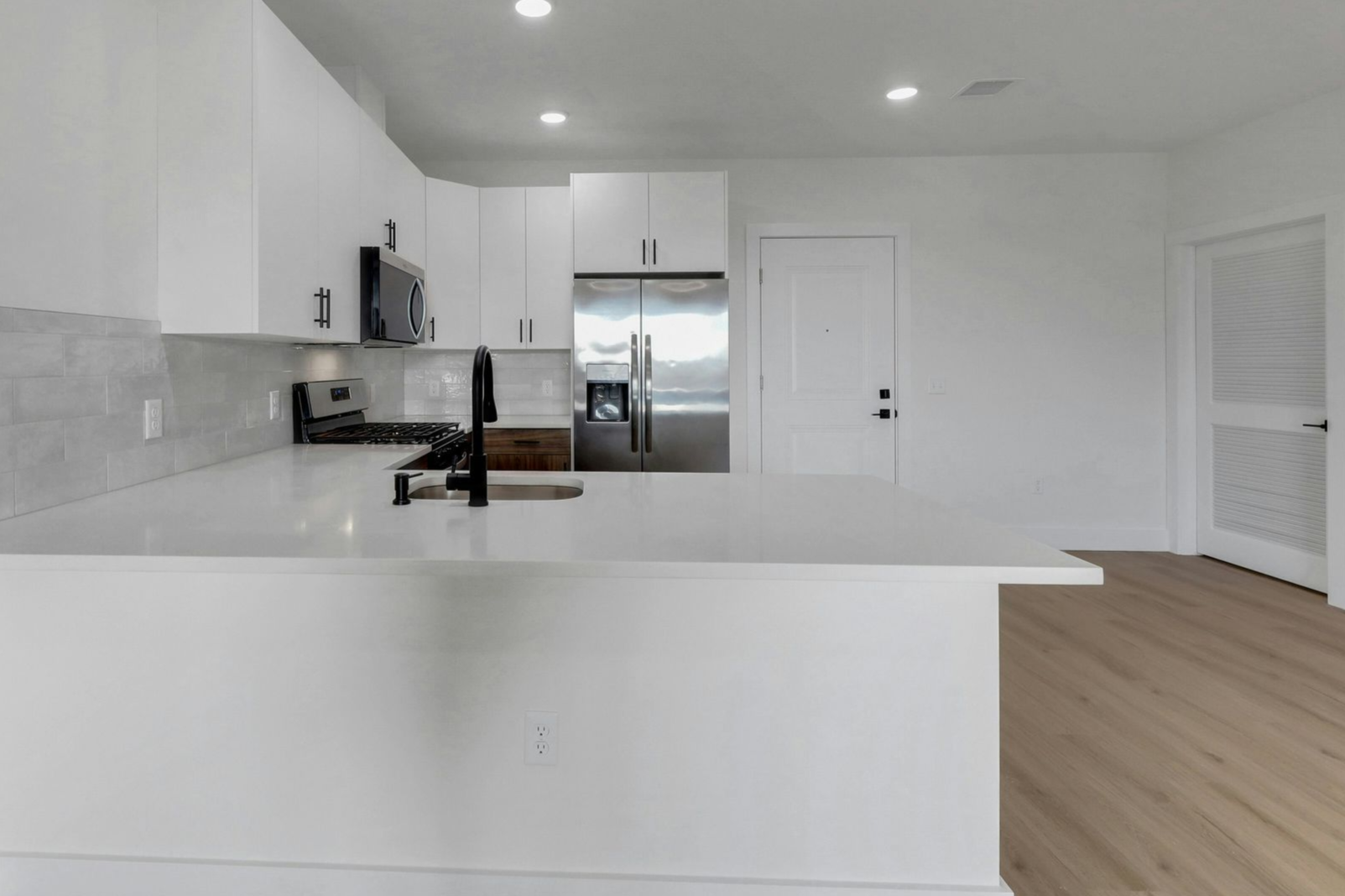 Modern white kitchen with a stainless steel refrigerator, white countertops, and a black faucet.