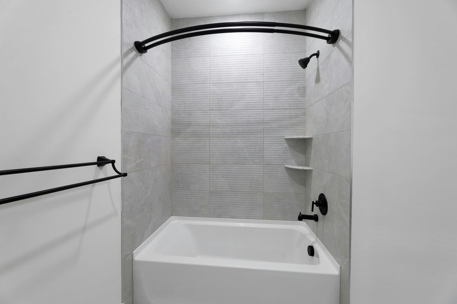 Bathroom with white tub, light gray tile, black fixtures, and a curved shower rod.