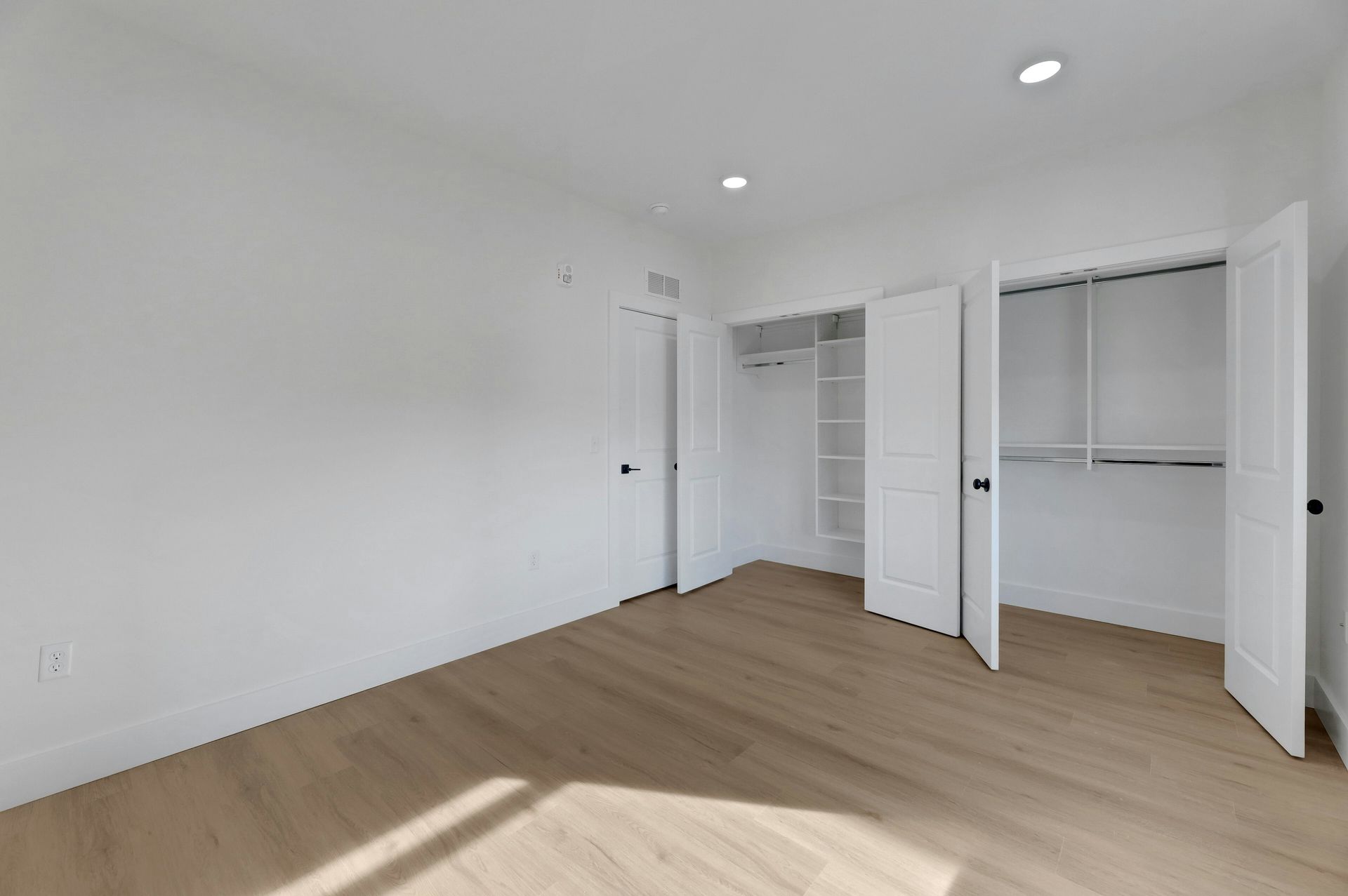 Empty bedroom with white walls, wood floor, and two closets.