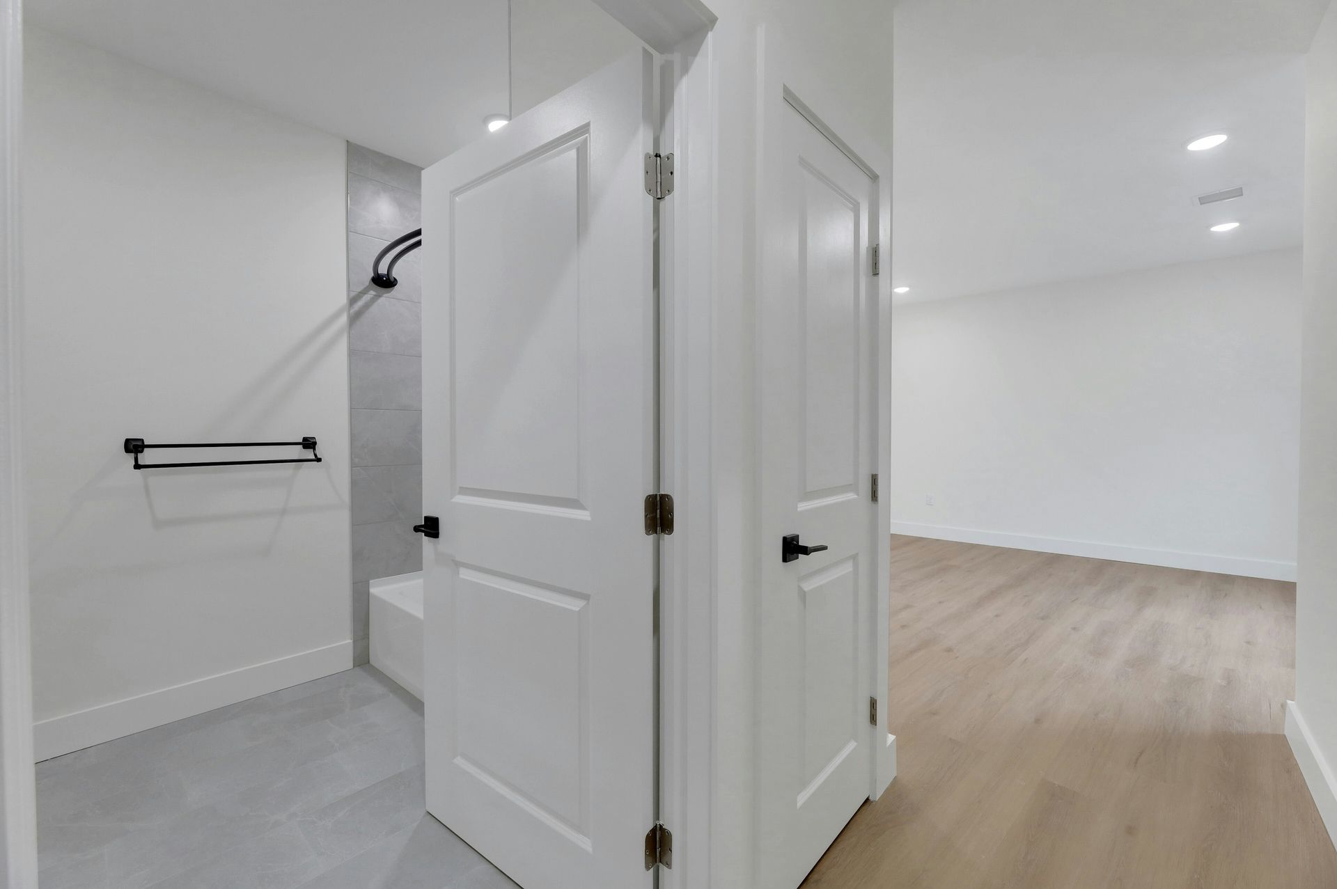 Hallway with white doors, one leading to a bathroom with gray tiles and a towel rack.