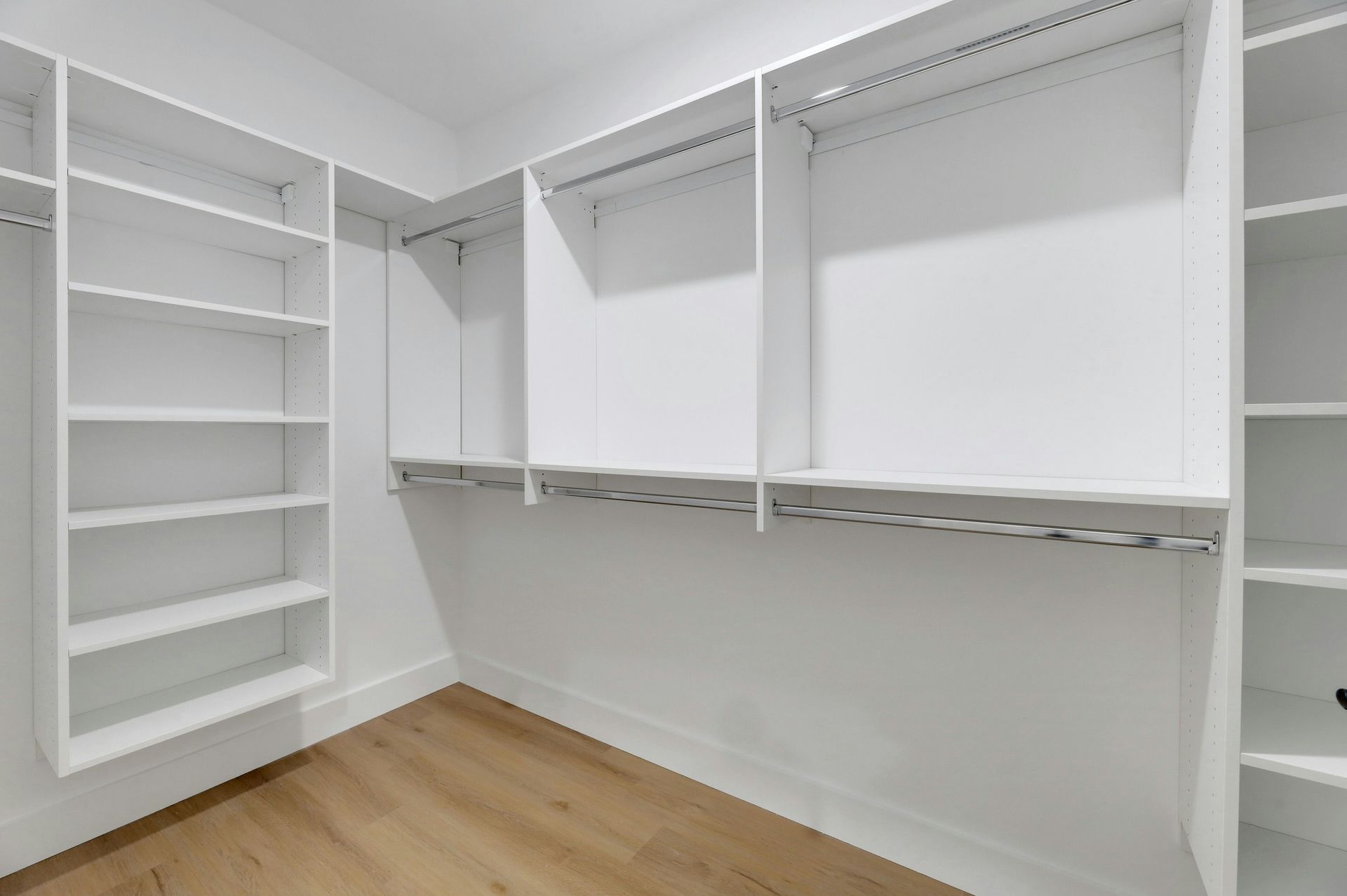 Empty white closet with shelving, rods, and wooden floor.