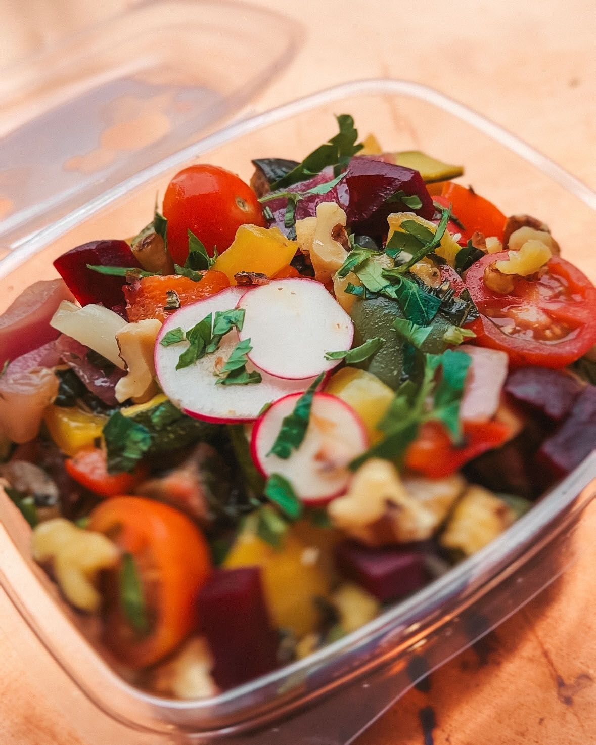 a salad in a plastic container with tomatoes radishes and other vegetables