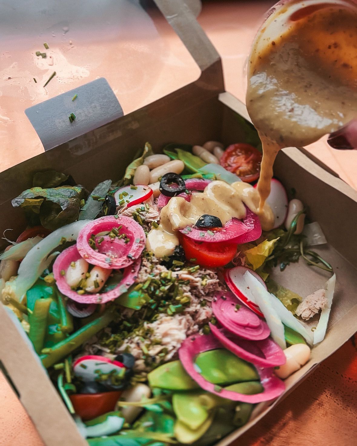 a person is pouring dressing on a salad in a cardboard box