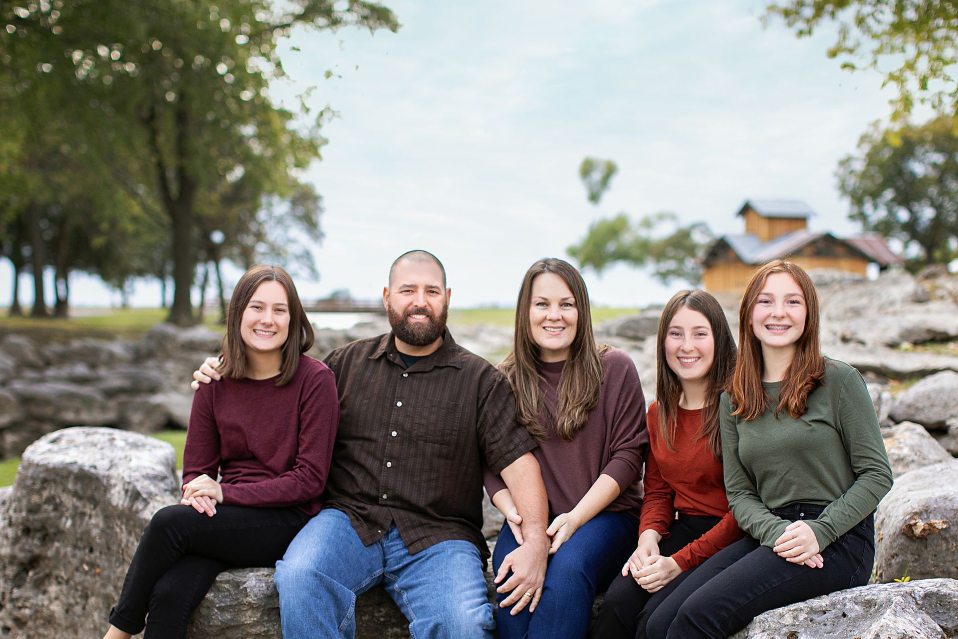 Family of five sitting on rocks outdoors, smiling.