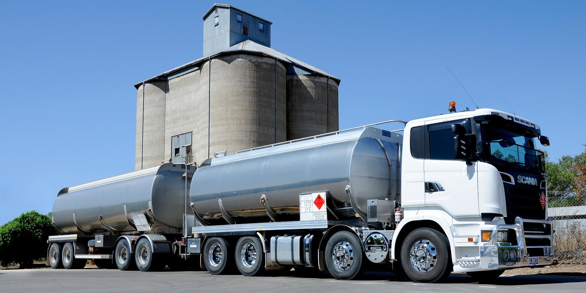 A large tanker truck is parked in front of a silo.