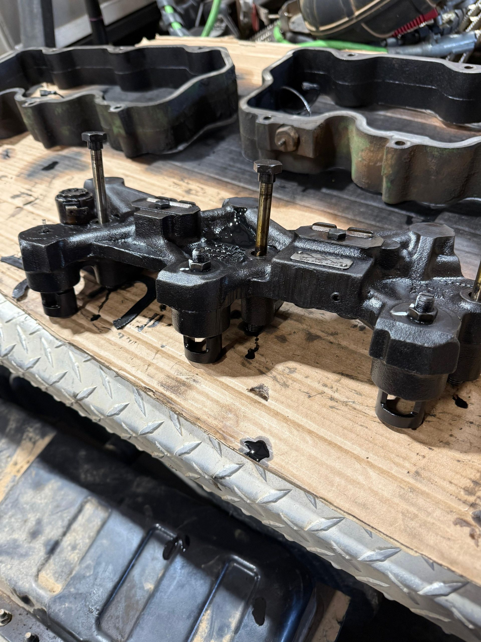 A black, oily engine component on a wooden surface with two other components visible in the background.