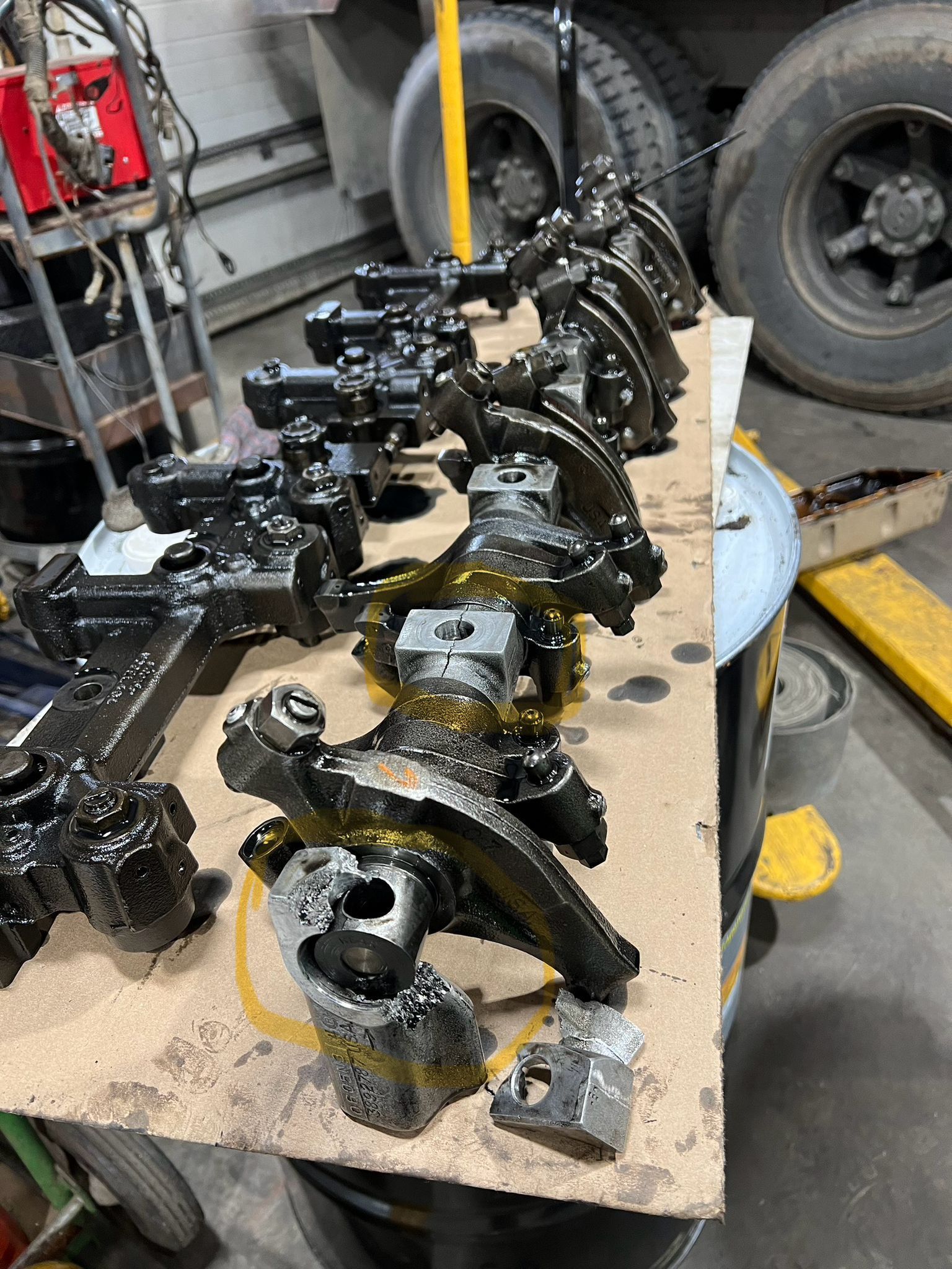 Engine parts arranged on a cardboard sheet, oily and dark, in a workshop setting.
