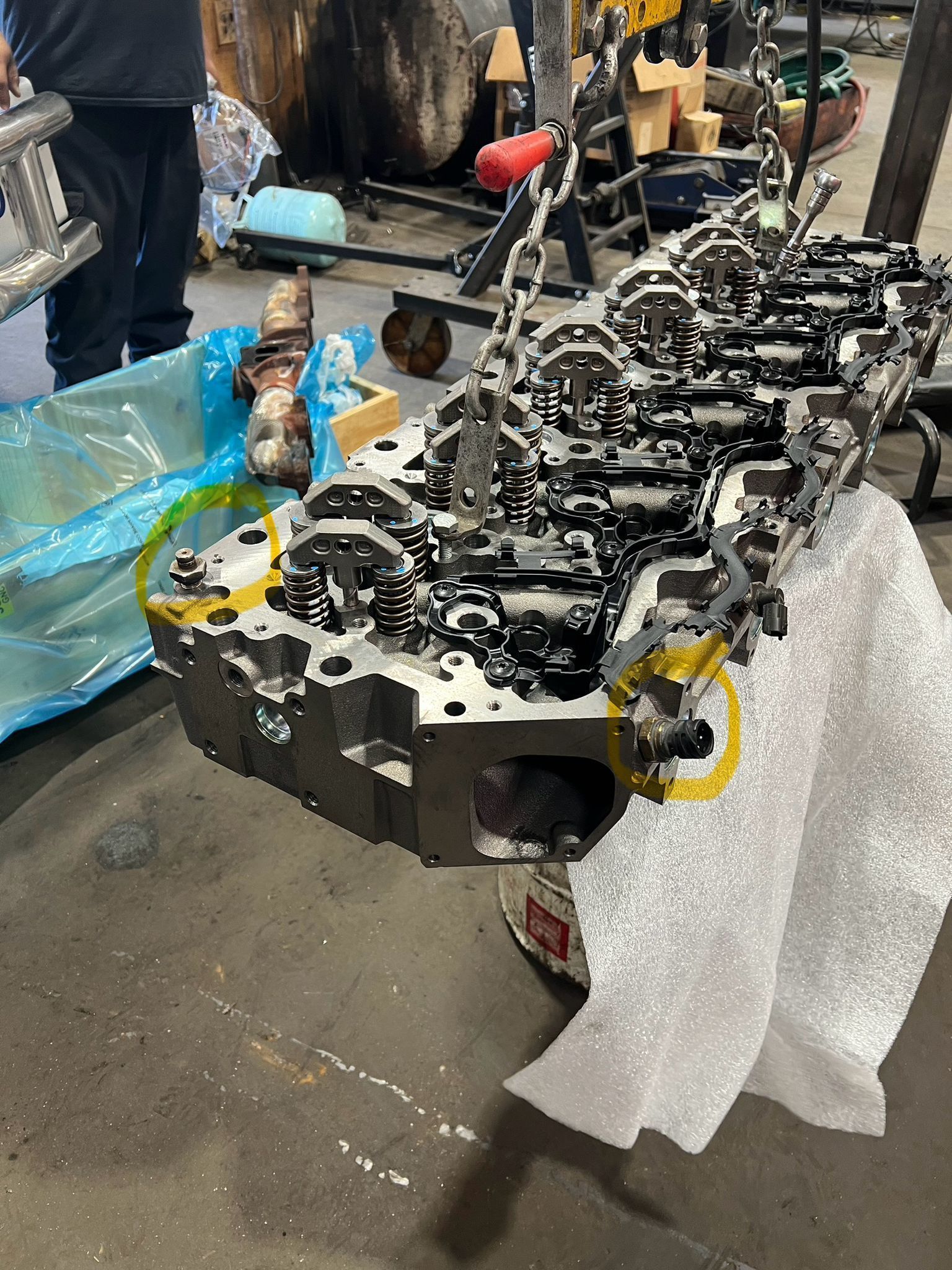 Engine block on a workbench, covered in foam, with a person and shop equipment in the background.