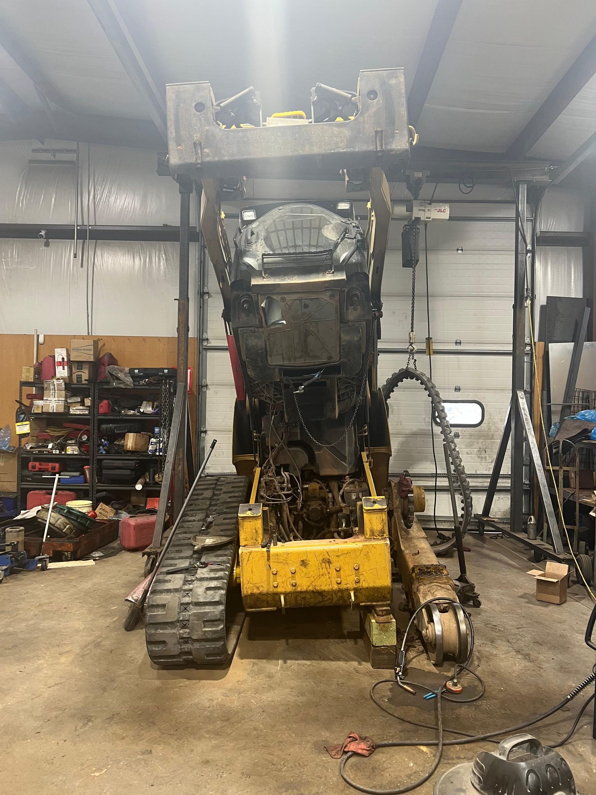 Yellow skid steer loader with grapple attachment inside a workshop.