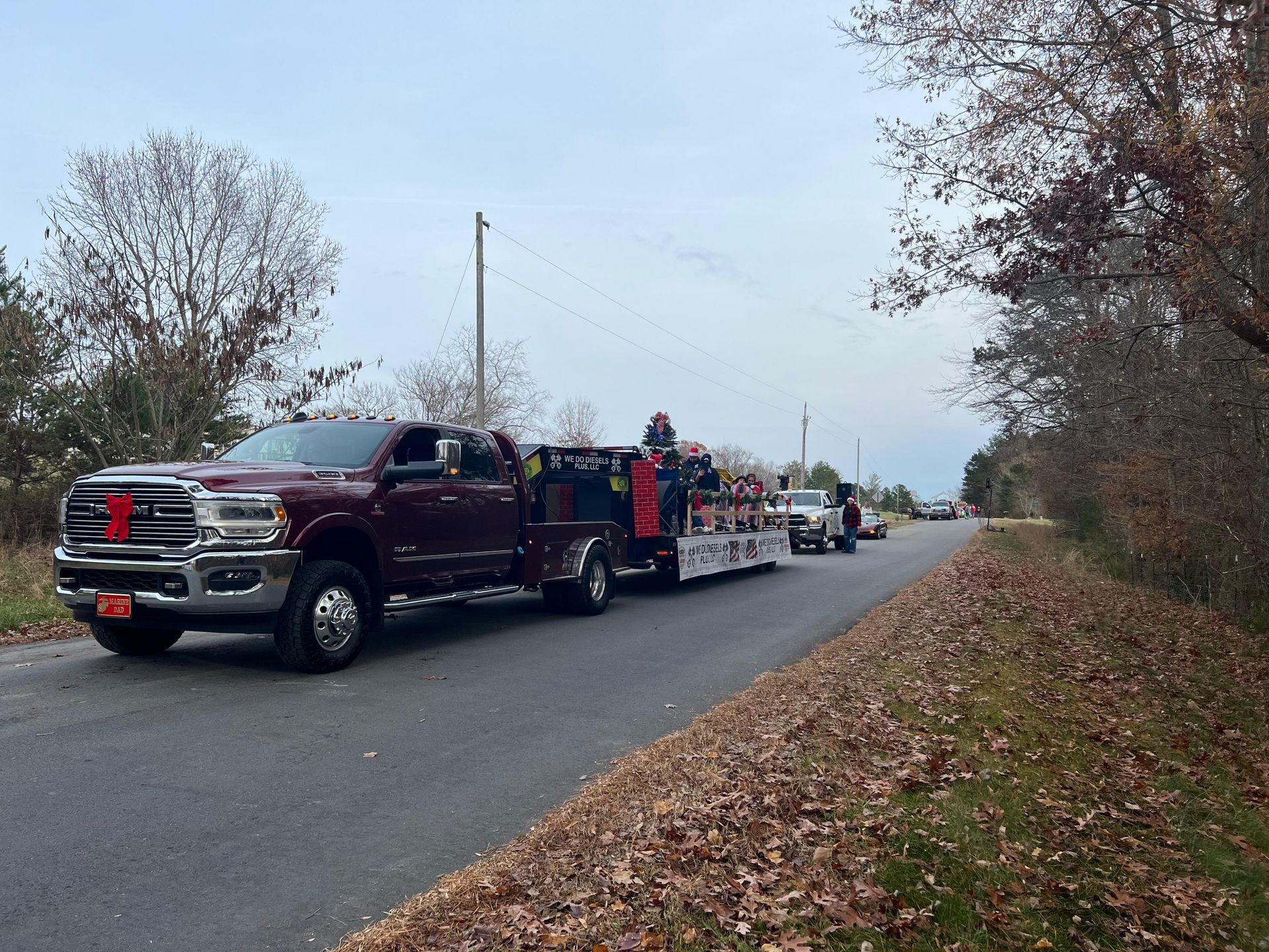 Maroon pickup truck towing trailer with items, on a road with trees.