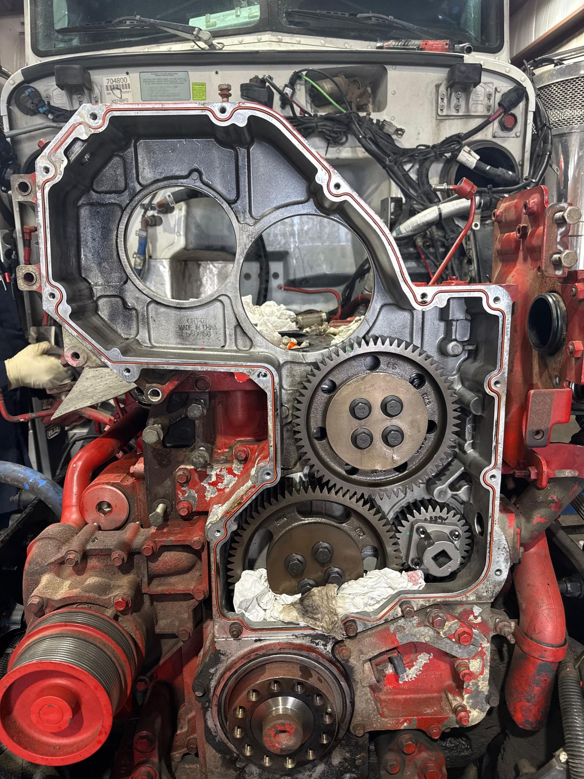 Truck engine with open timing cover, revealing gears and red components.