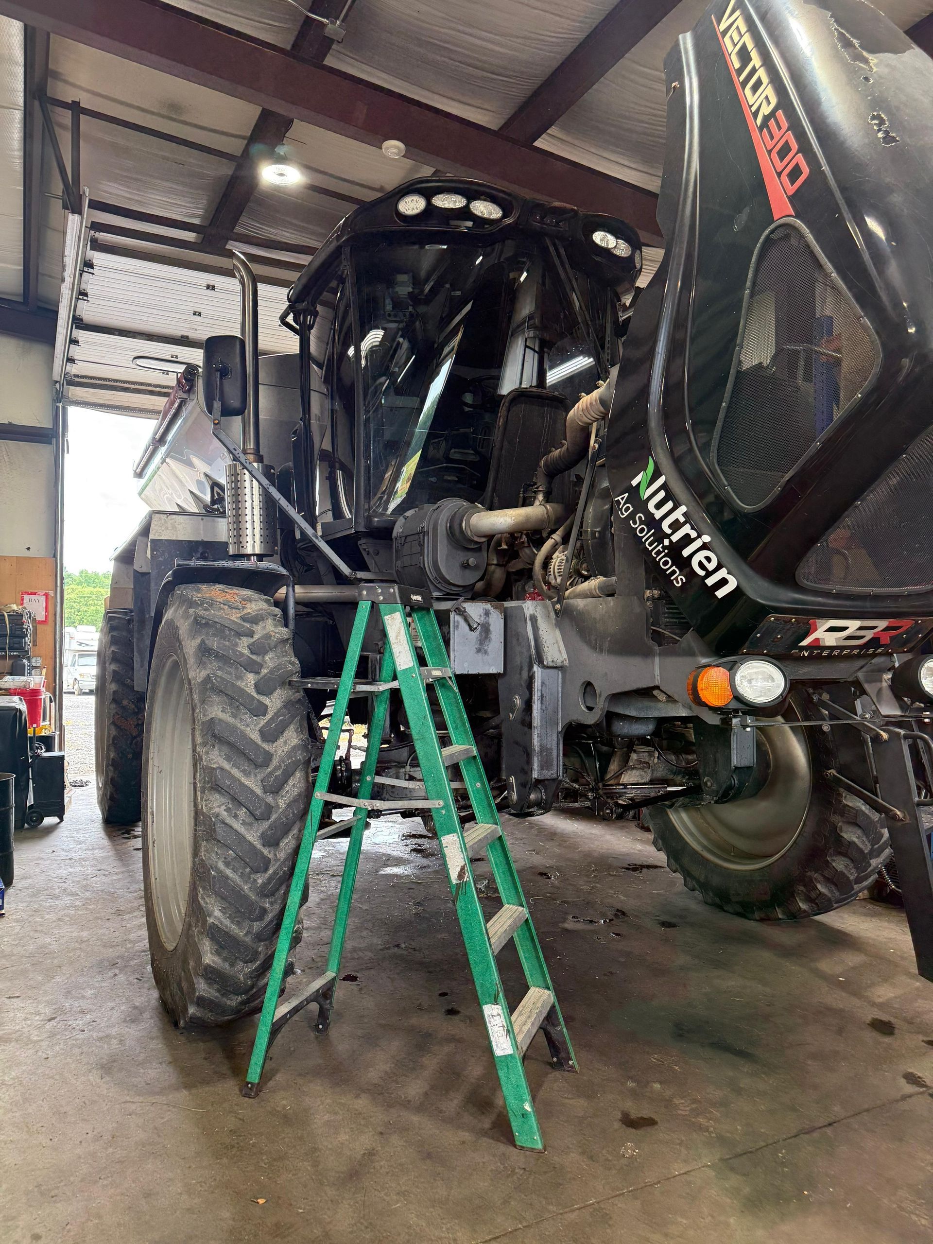 Black agricultural sprayer with hood open, ladder in front.