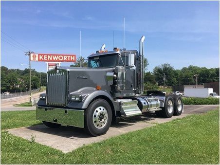Gray Kenworth semi-truck parked in front of a Kenworth sign on a sunny day.