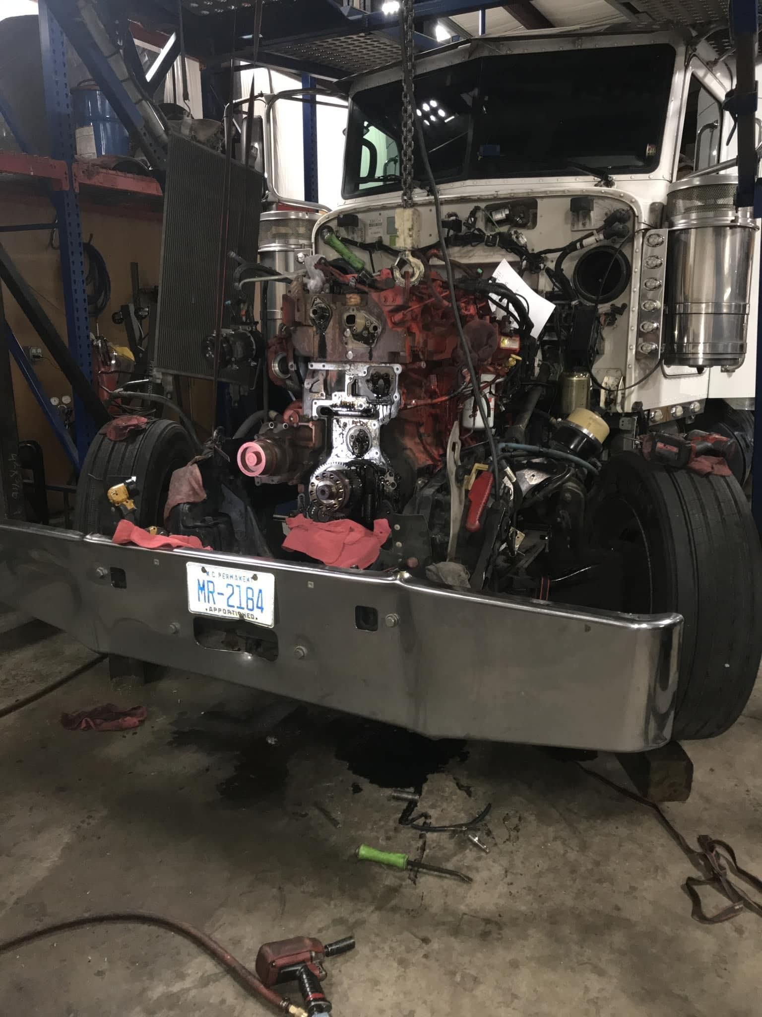 Truck undergoing repair in a garage, engine exposed, front bumper removed.