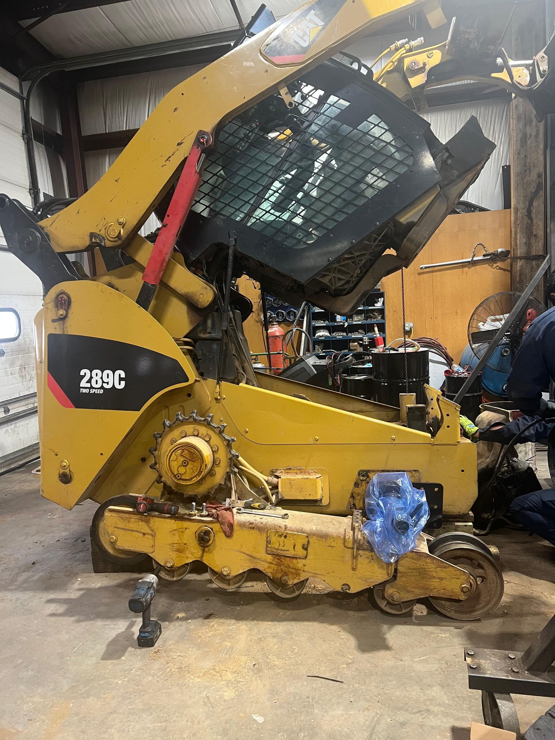 Yellow Caterpillar 289C skid steer with the cab raised in a repair shop.