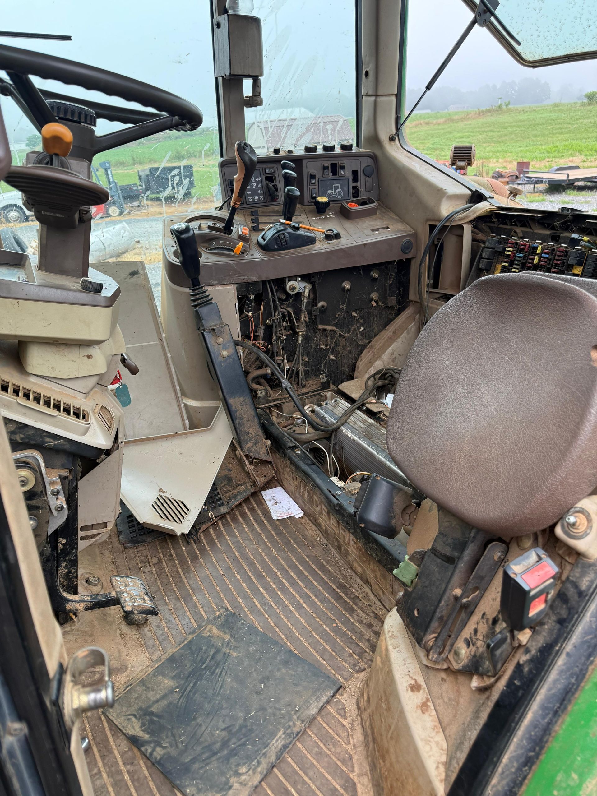 Interior of a dirty tractor cab with mud on floor, control panel, steering wheel, and seat visible.
