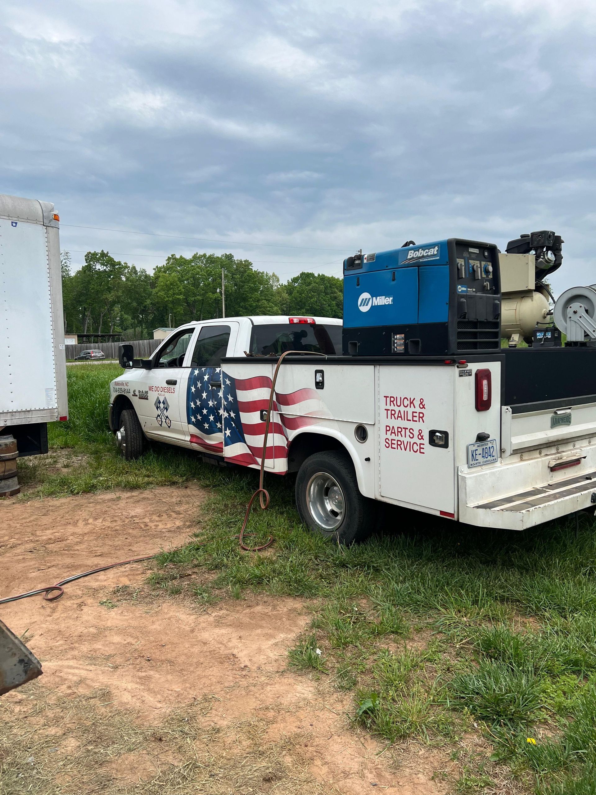 White pickup truck with American flag graphic and welding equipment, parked on grass.