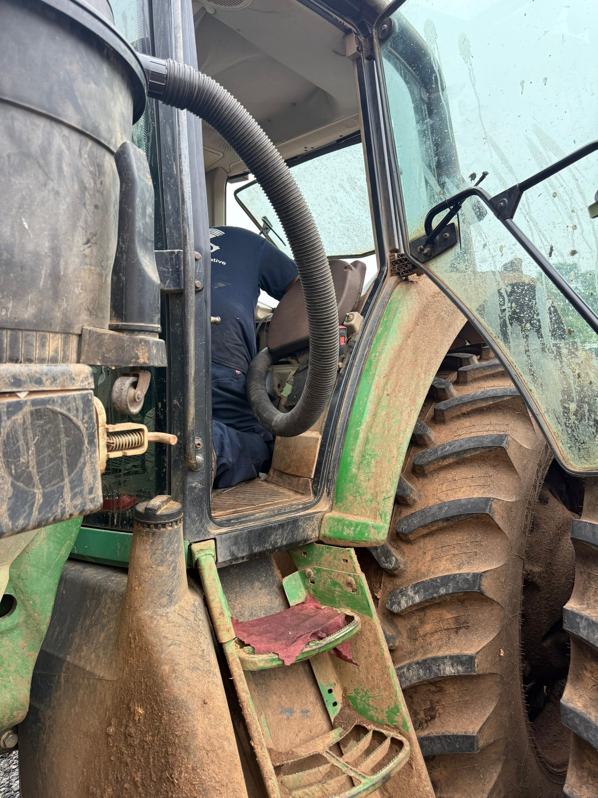 Person working on the interior of a green tractor, muddy exterior, side view.