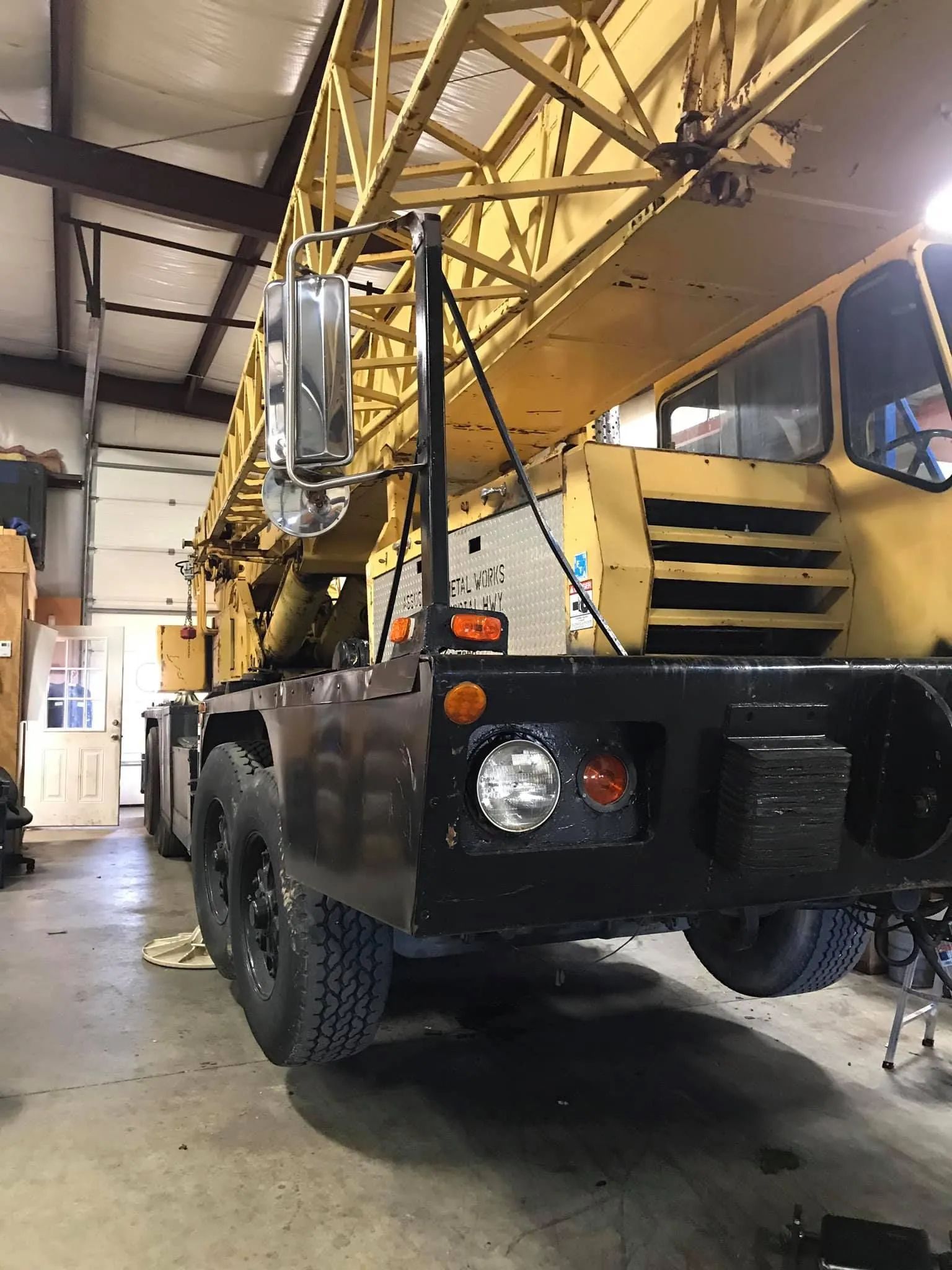 Yellow construction crane in a garage, black chassis, tires, and lights.