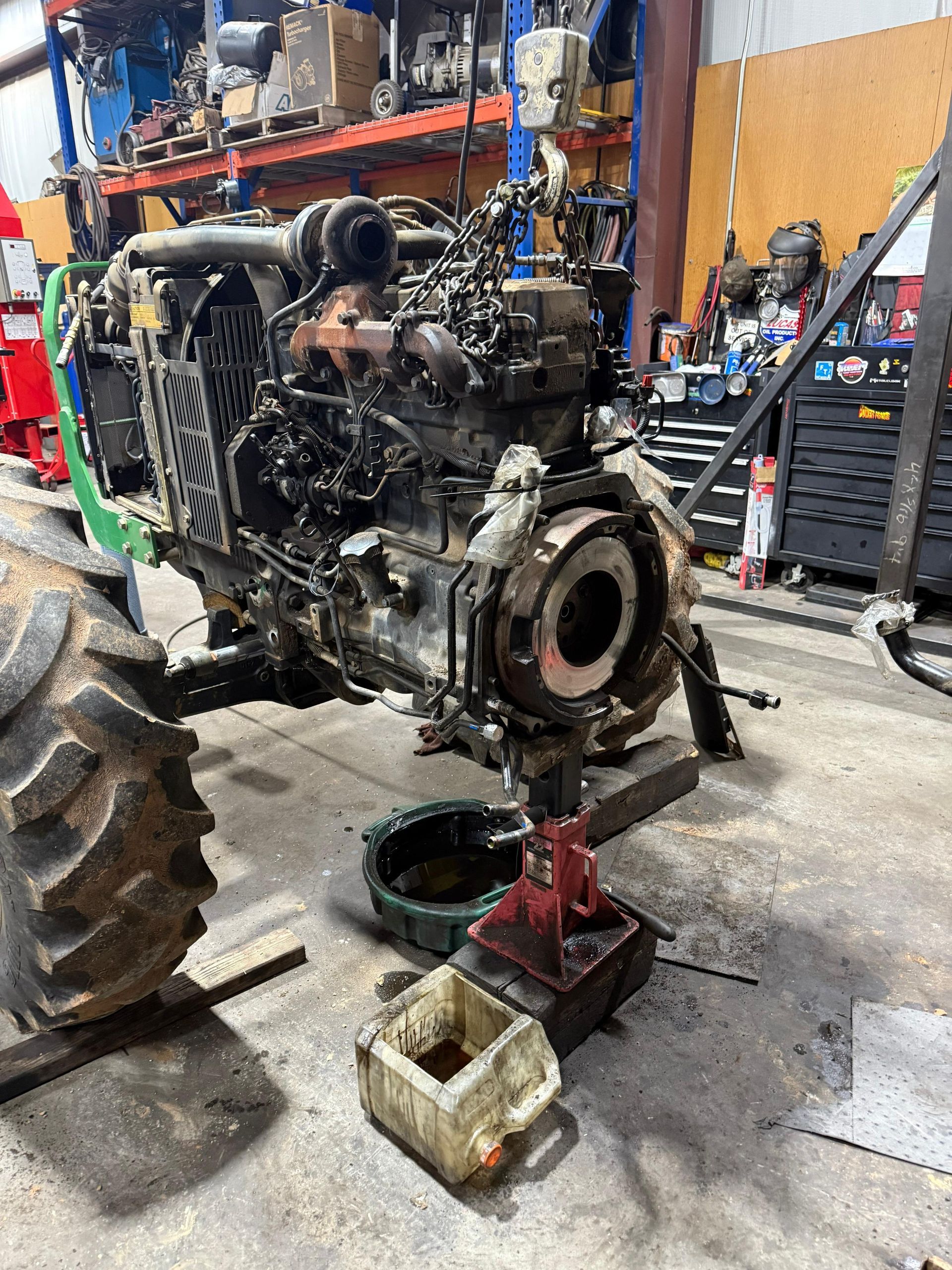 Tractor engine being repaired in a workshop with tools and oil drain.