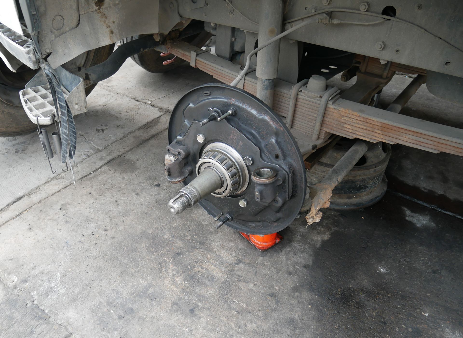 Rear truck wheel assembly, tire removed, on a concrete surface, with suspension visible.