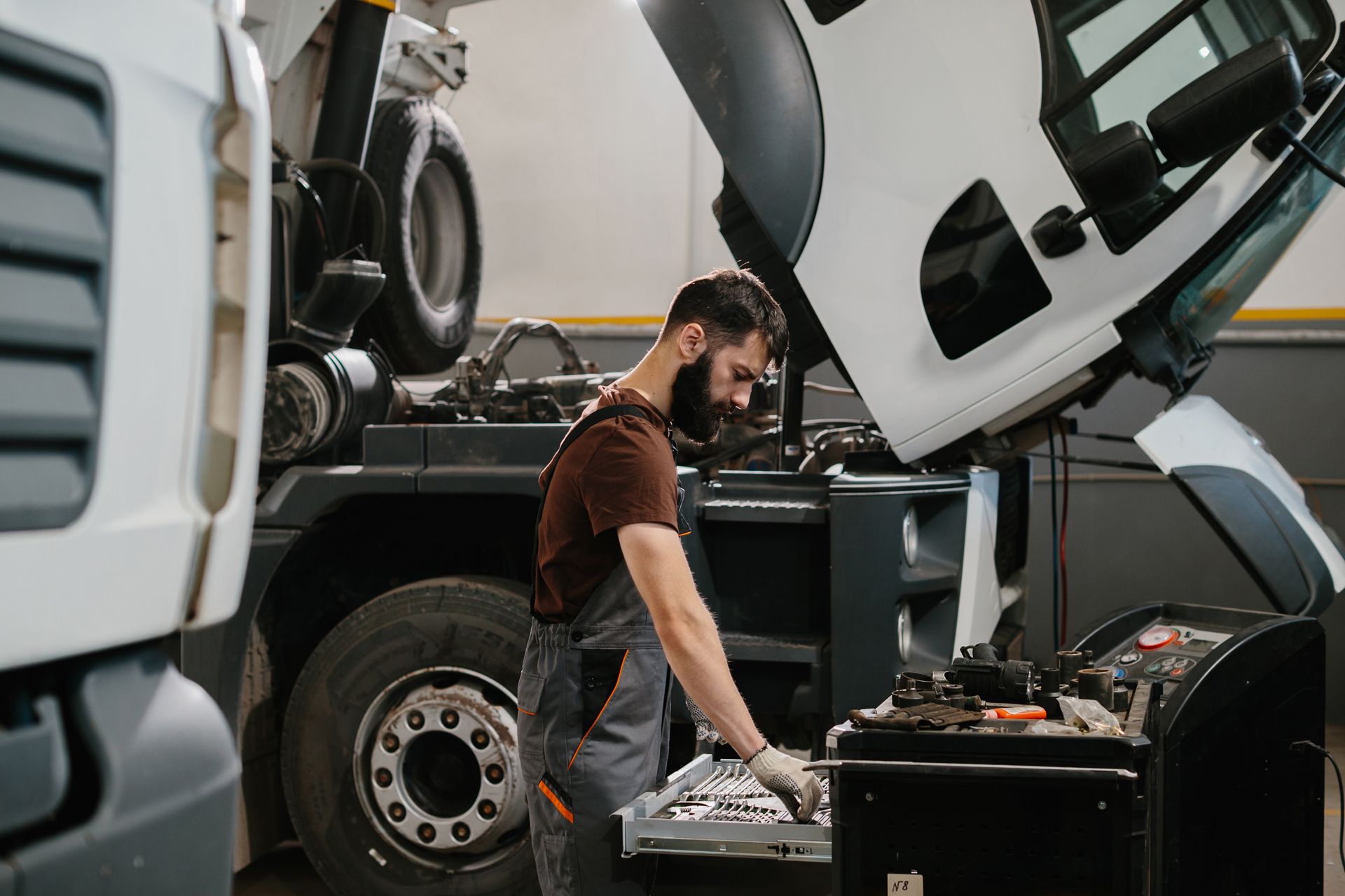 Person in green jacket inspecting semi-truck tires, holding clipboard.