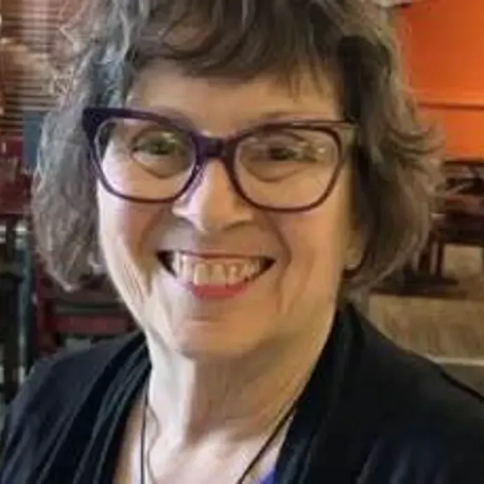 Woman with glasses smiles; black top, restaurant setting.