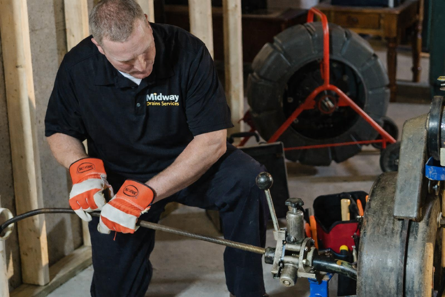 A person in a blue uniform repairing a sink drain underneath a kitchen cabinet with tools nearby.
