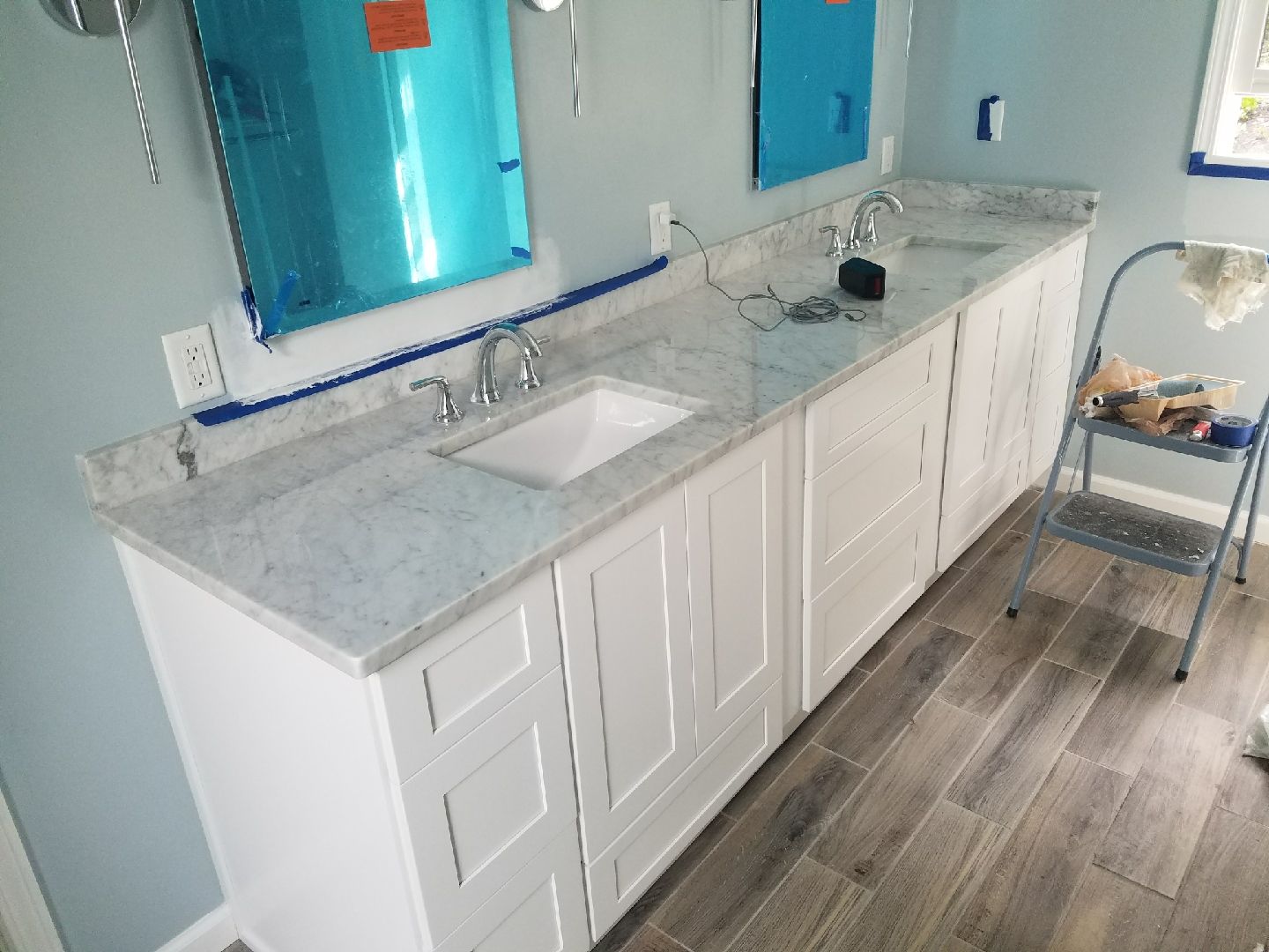 White bathroom vanity with two sinks, gray countertop, blue mirrors, and light blue walls.