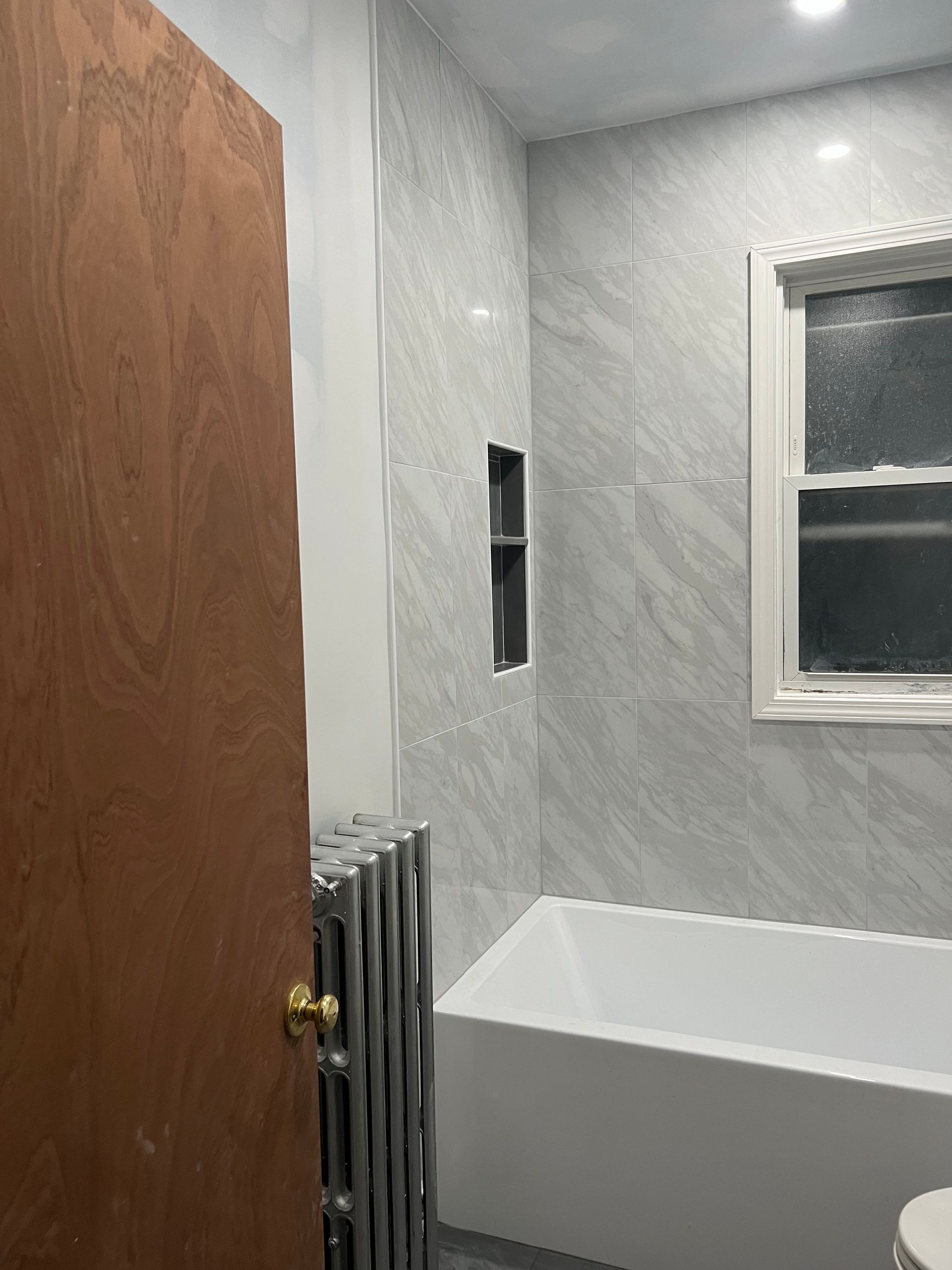 A bathroom with a tub , toilet , and window.