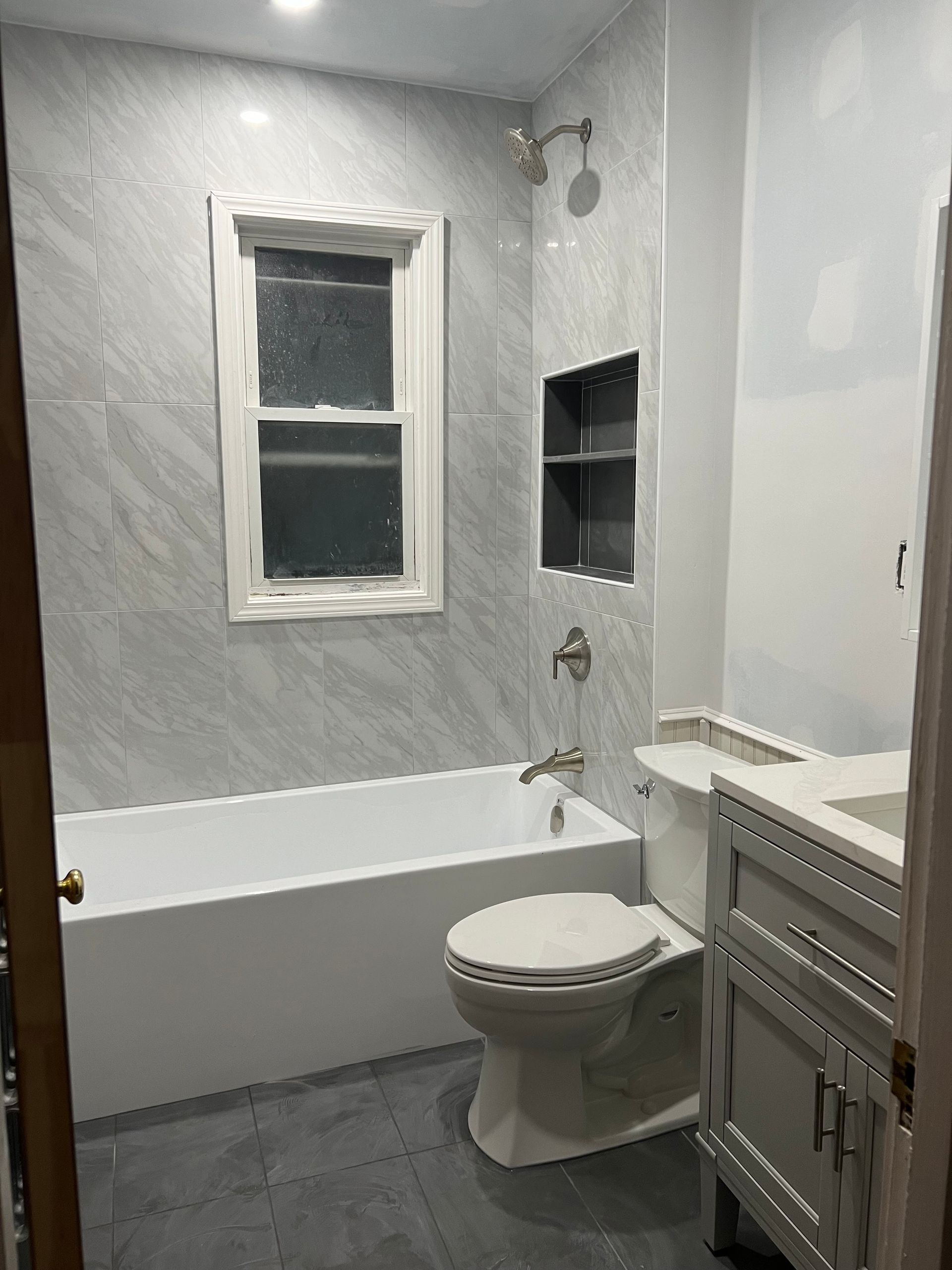 A bathroom with a toilet , sink , bathtub and window.