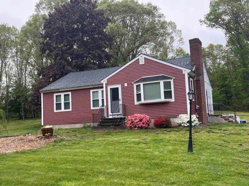 A red house with a black roof is sitting on top of a lush green field.