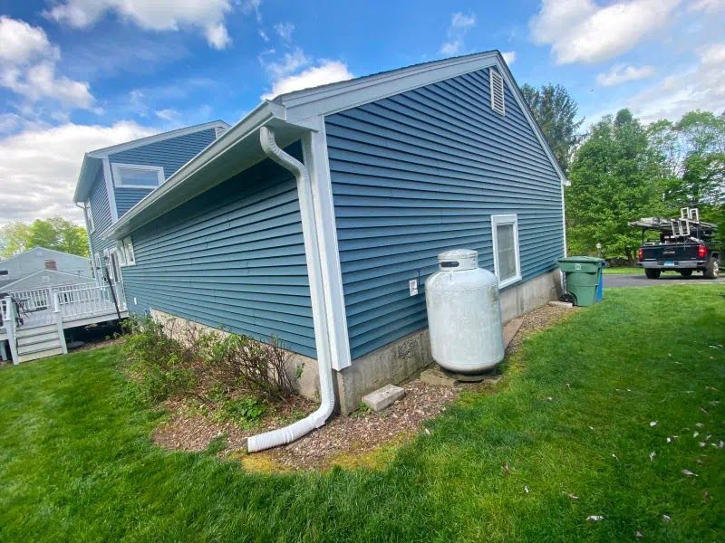 A blue house with a white propane tank on the side of it.