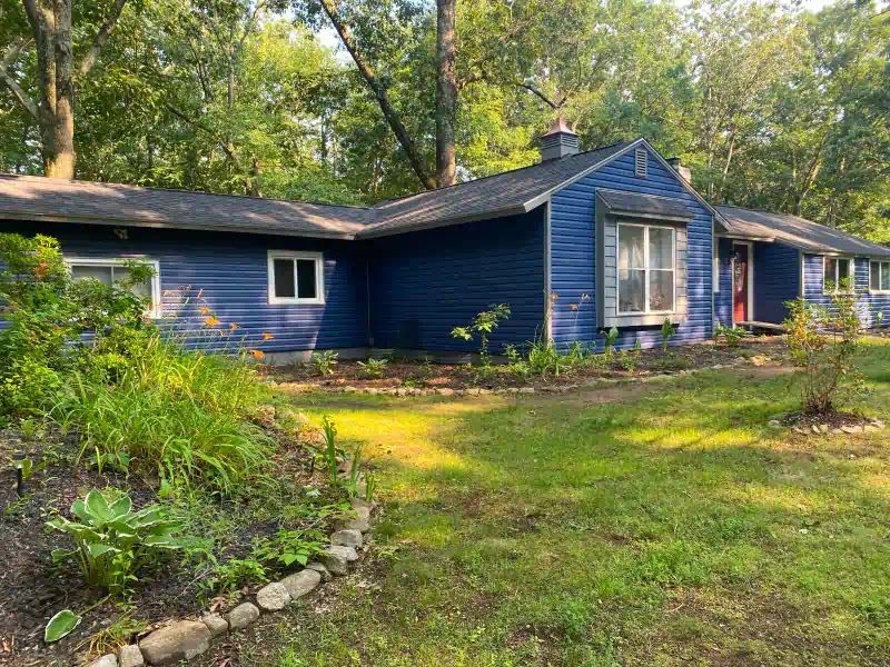 A blue house with a lush green yard and trees in the background.