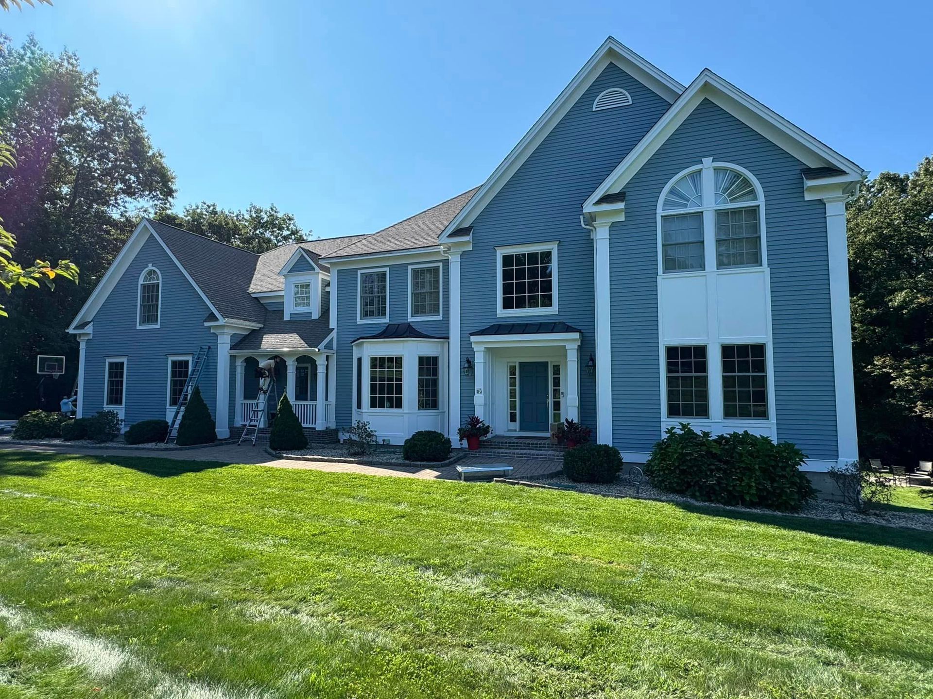 A large blue and white house with a lush green lawn in front of it