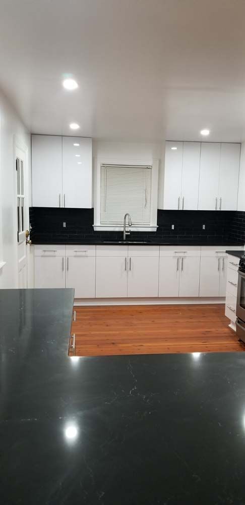A kitchen with white cabinets, black backsplash, and black countertop.