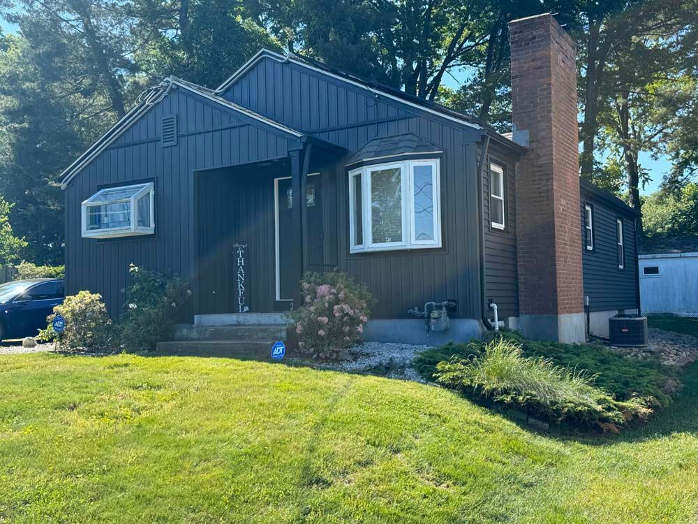 Dark blue house with white trim, bay window, and a brick chimney on a grassy lawn.
