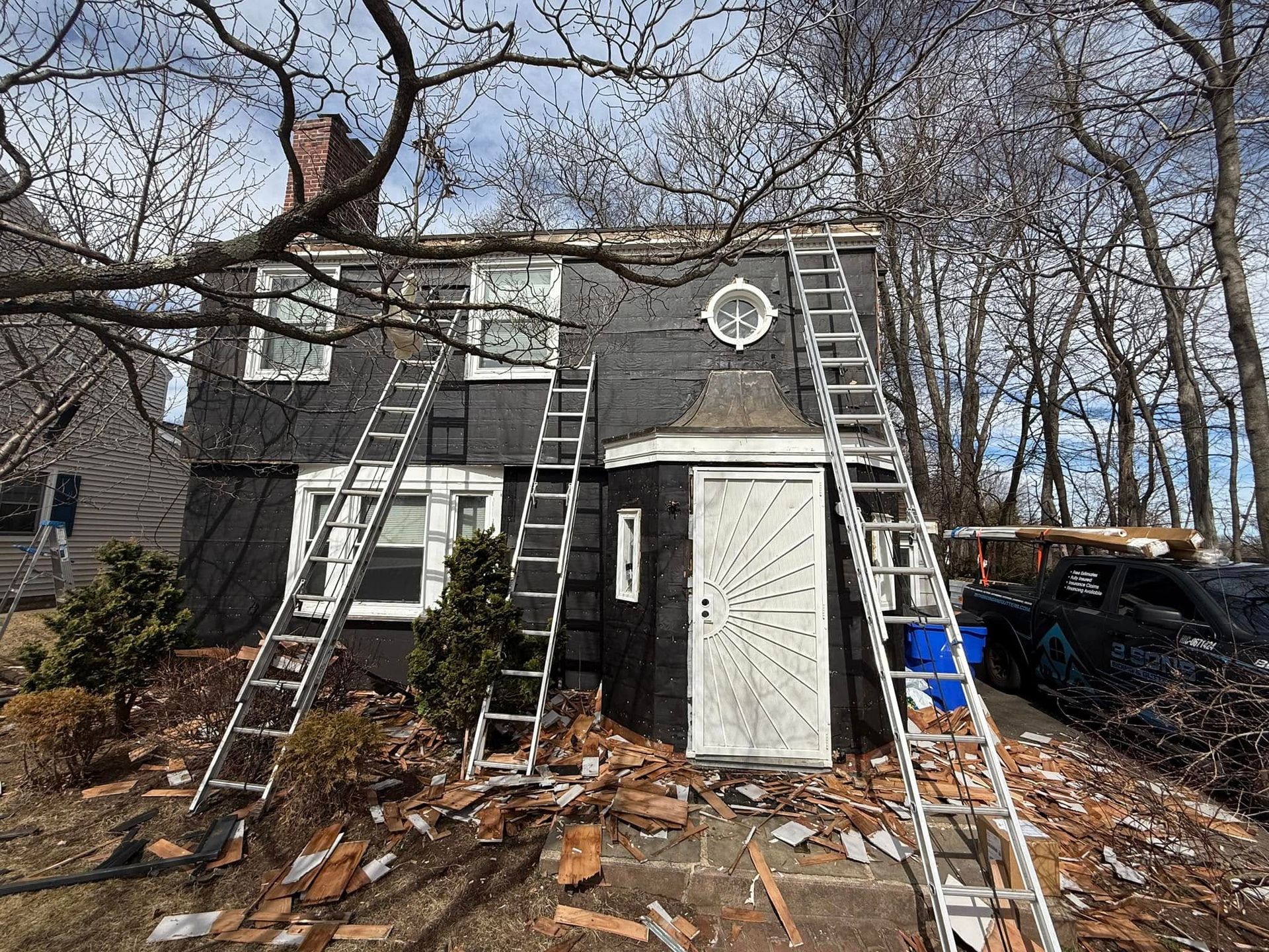 House with ladders leaning against it; roof being repaired with debris on the ground.