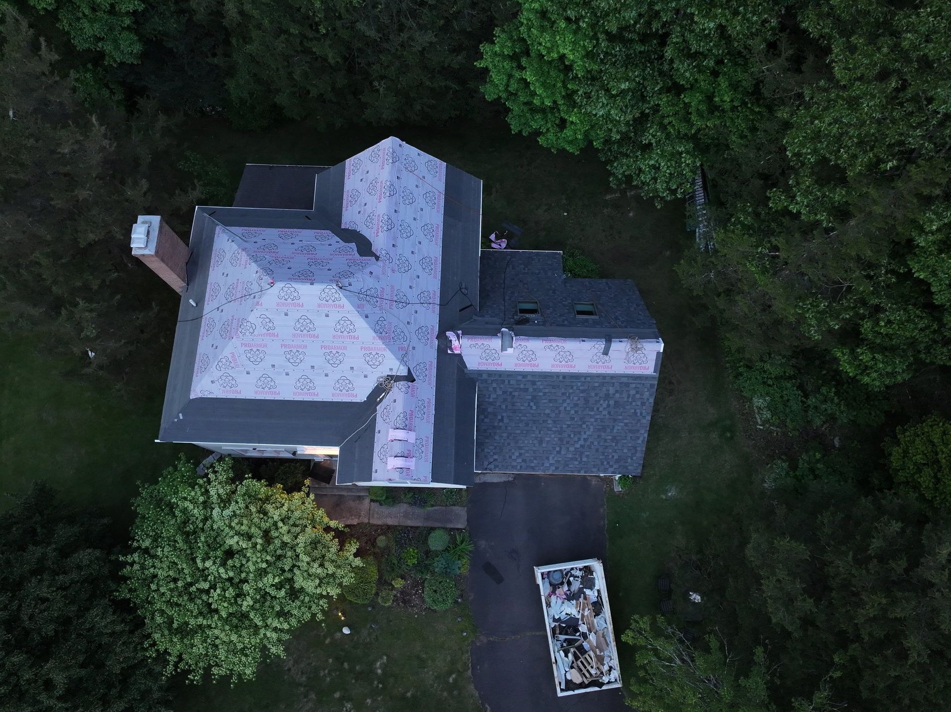 Overhead view of a house with a dark roof and a driveway with a vehicle. Surrounded by trees.