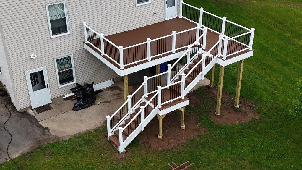 Brown and white multi-level deck with stairs attached to a beige house, surrounded by green grass.