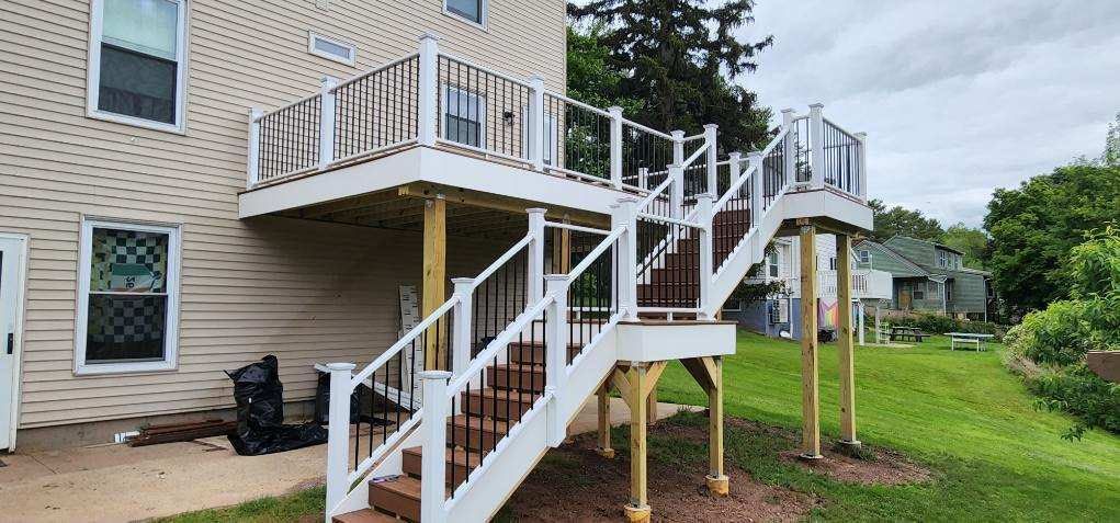 A two-story deck with stairs leading down to a grassy yard. The deck has white railings and brown steps.