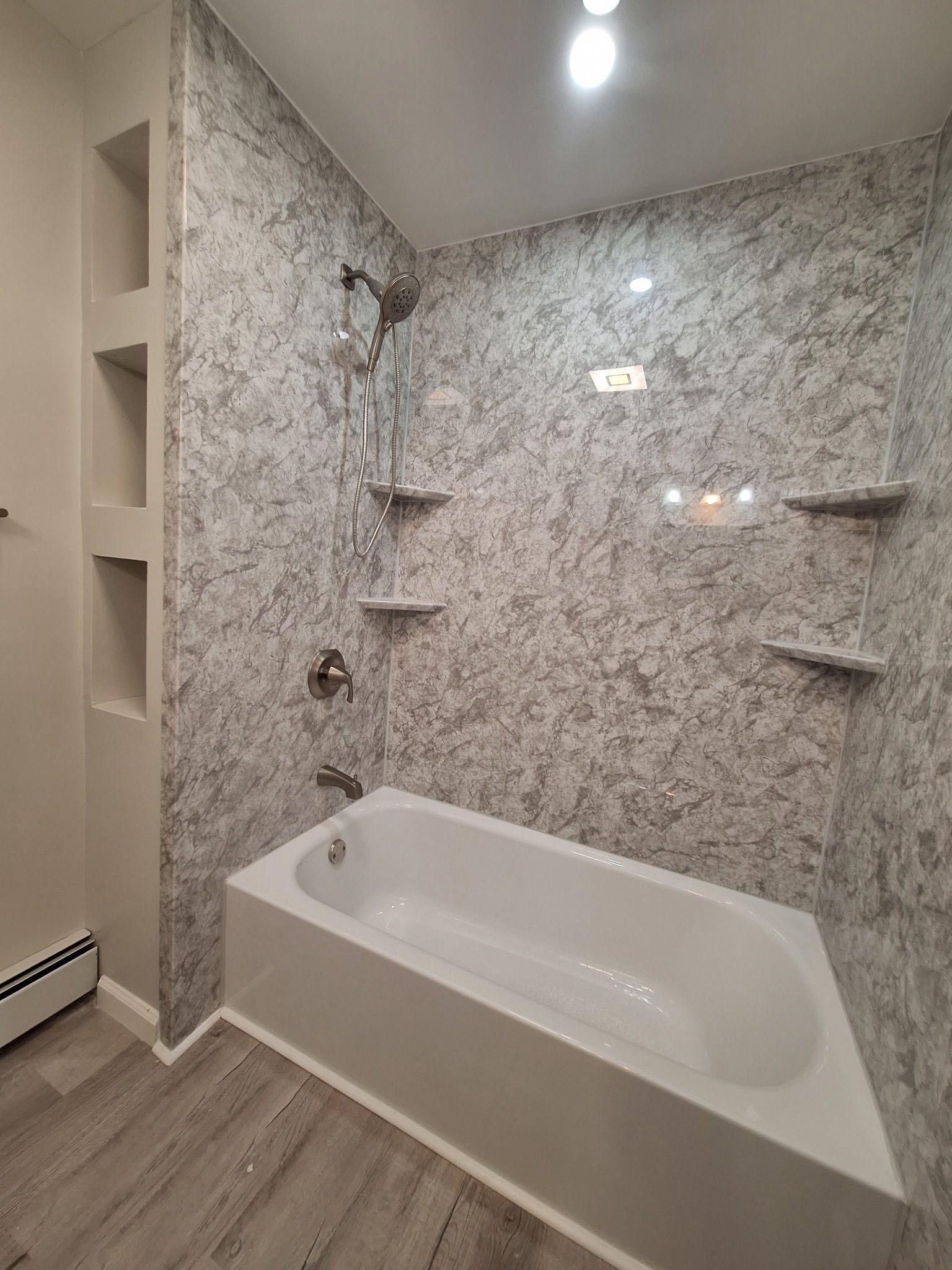 Bathroom with white tub, gray patterned walls, and recessed shelves.