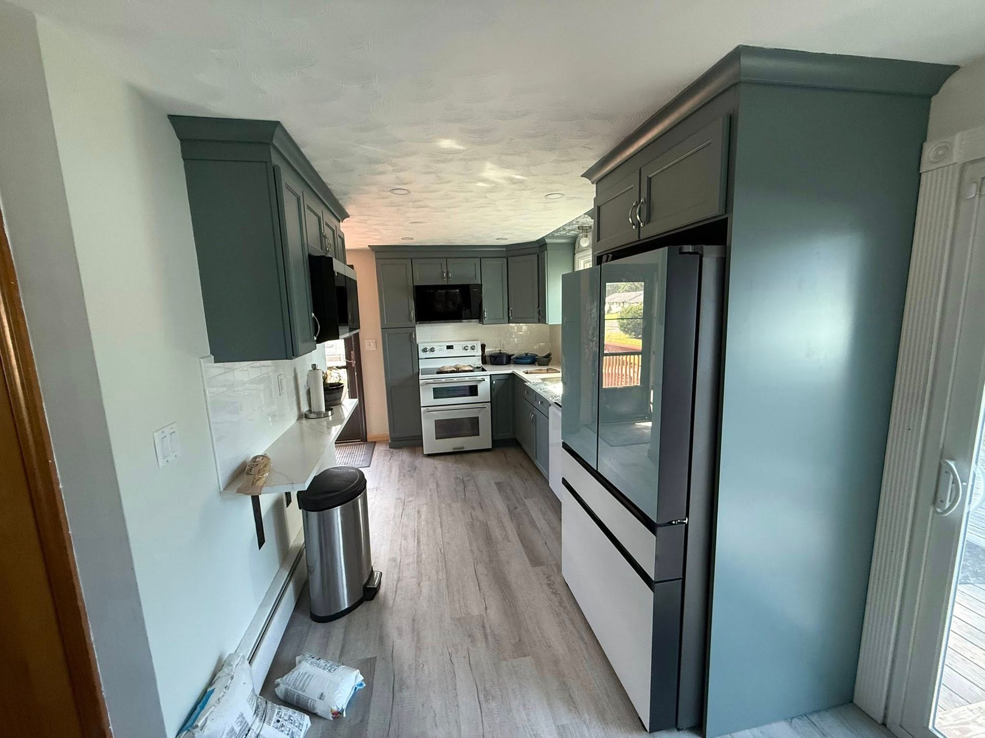 A kitchen with blue-green cabinets, a refrigerator, stove, and a doorway to an outdoor space.