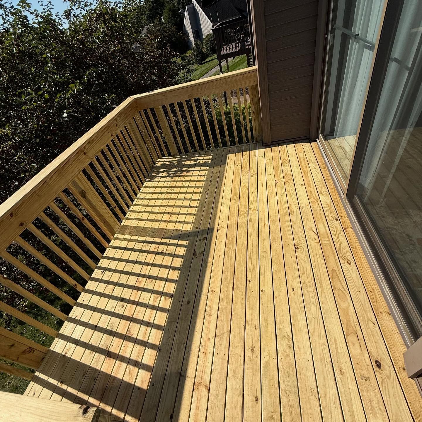 Wooden deck with railing, connected to a house with a sliding glass door.