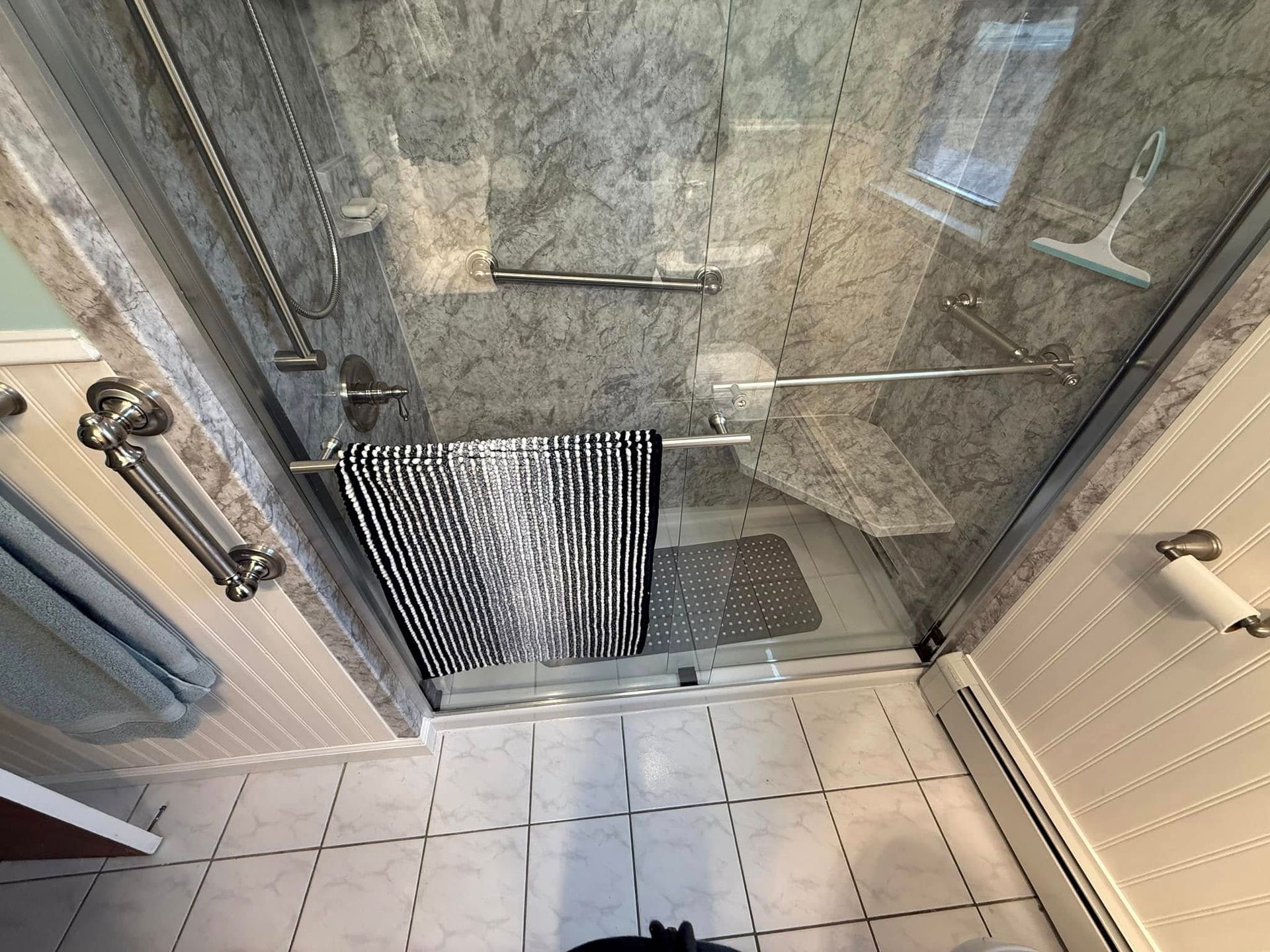 Shower stall with glass doors, gray tiled walls, and a towel rack holding a black and white striped towel.