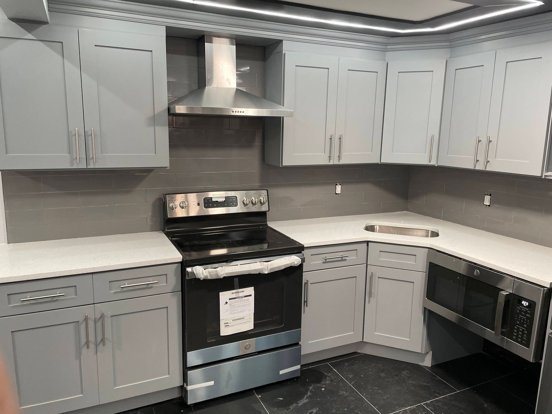Gray kitchen cabinets, stainless steel appliances, white countertops, and dark tile flooring.